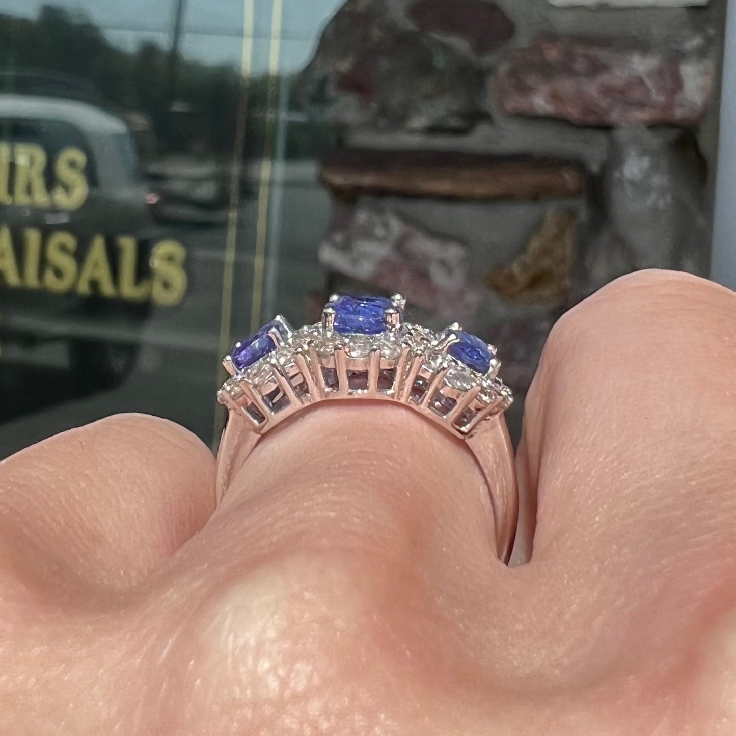 A sterling silver past, present, future three stone tanzanite ring. The main stones are set in a halo of cubic zirconia.