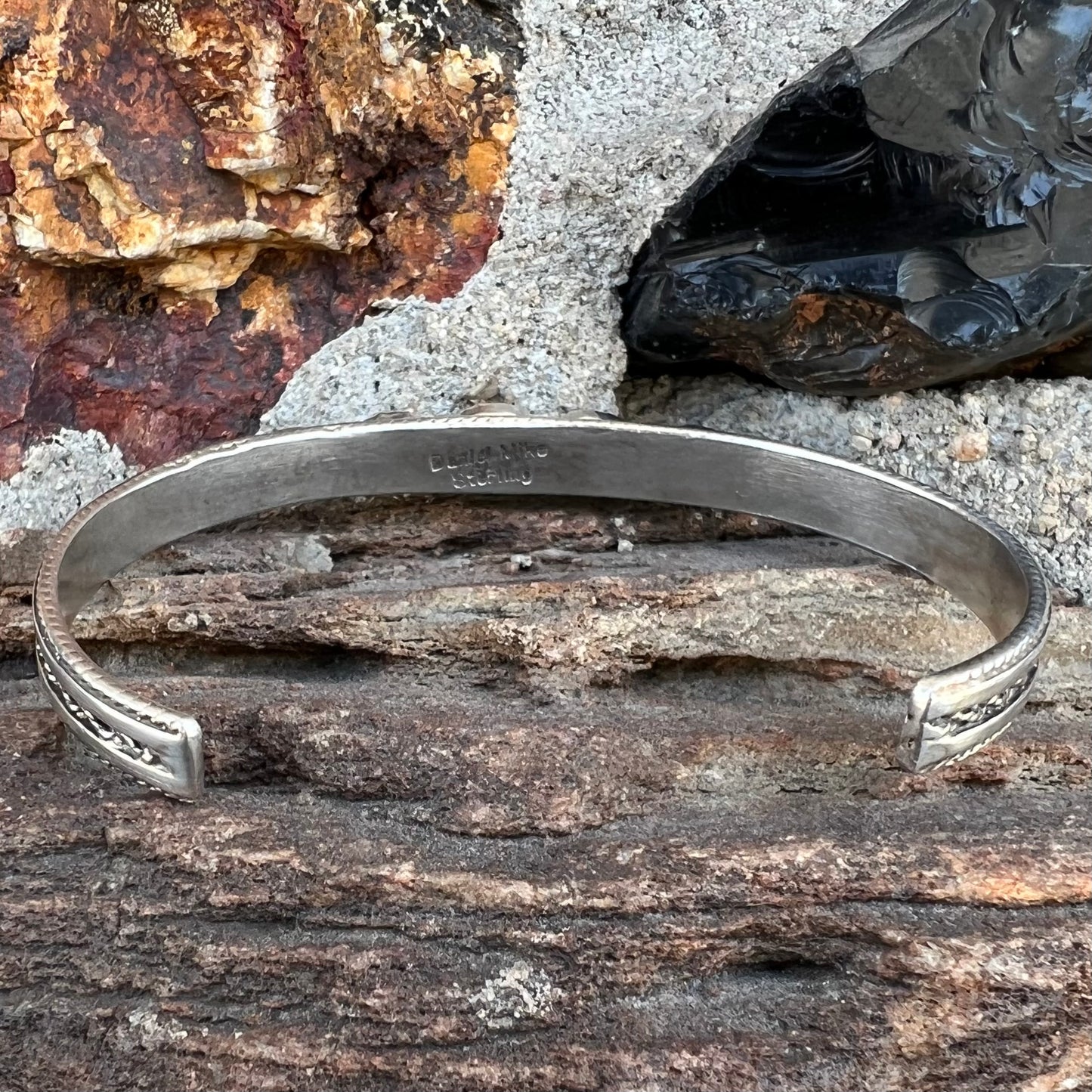 A silver rope cuff bracelet set with coral, turquoise, gaspeite, and lapis lazuli stones. The underside is stamped "Daniel Mike".