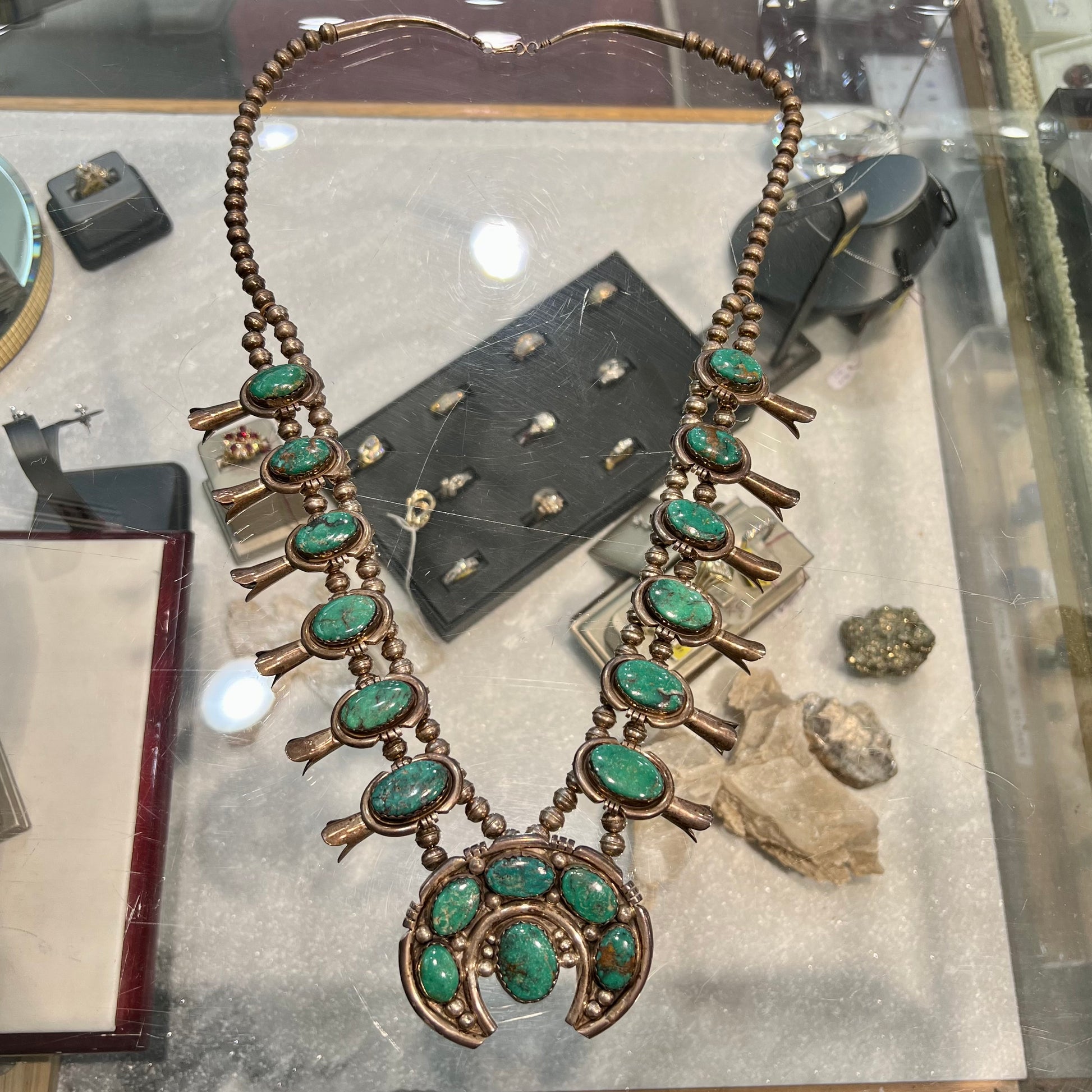 A silver Kingman turquoise squash blossom necklace.  The necklace is made with handmade Navajo pearls.