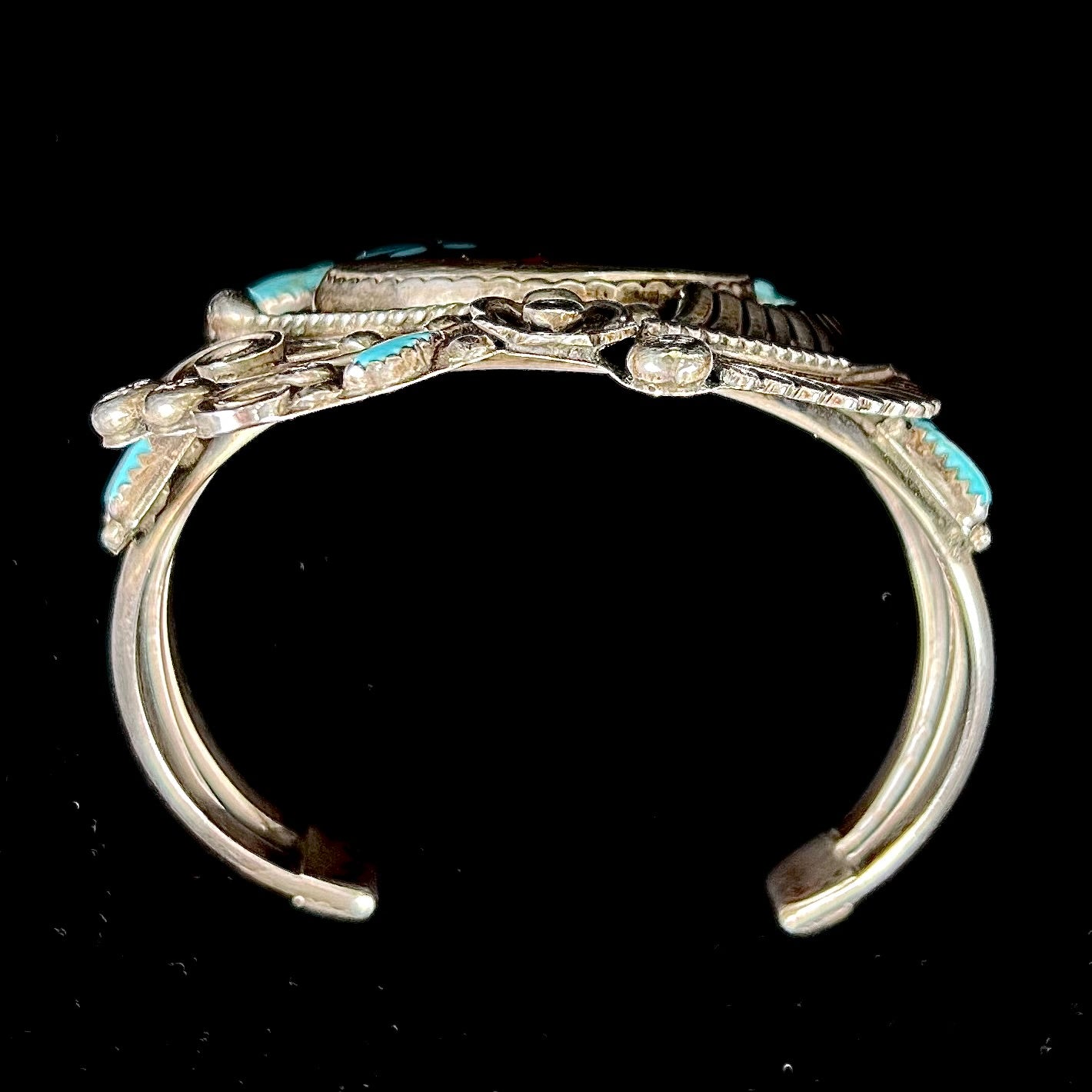A sterling silver cuff bracelet featuring the motif of a stone inlaid hummingbird with petit point turquoise accents, handmade by Navajo artist Leo G. Harvey.