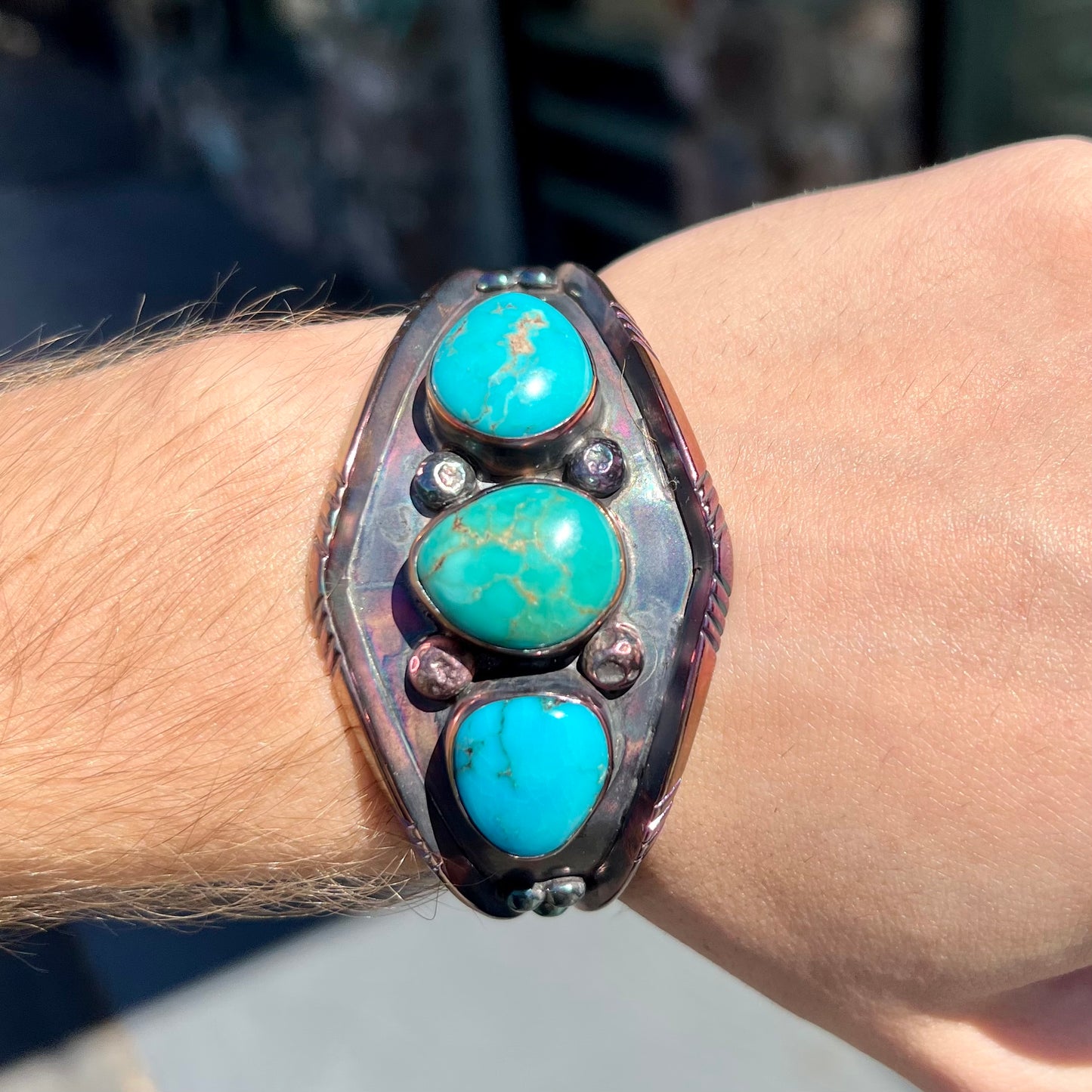 A men's Navajo three stone turquoise cuff bracelet handmade by artist, Dean Brown. The silver has an iridescent purple patina.