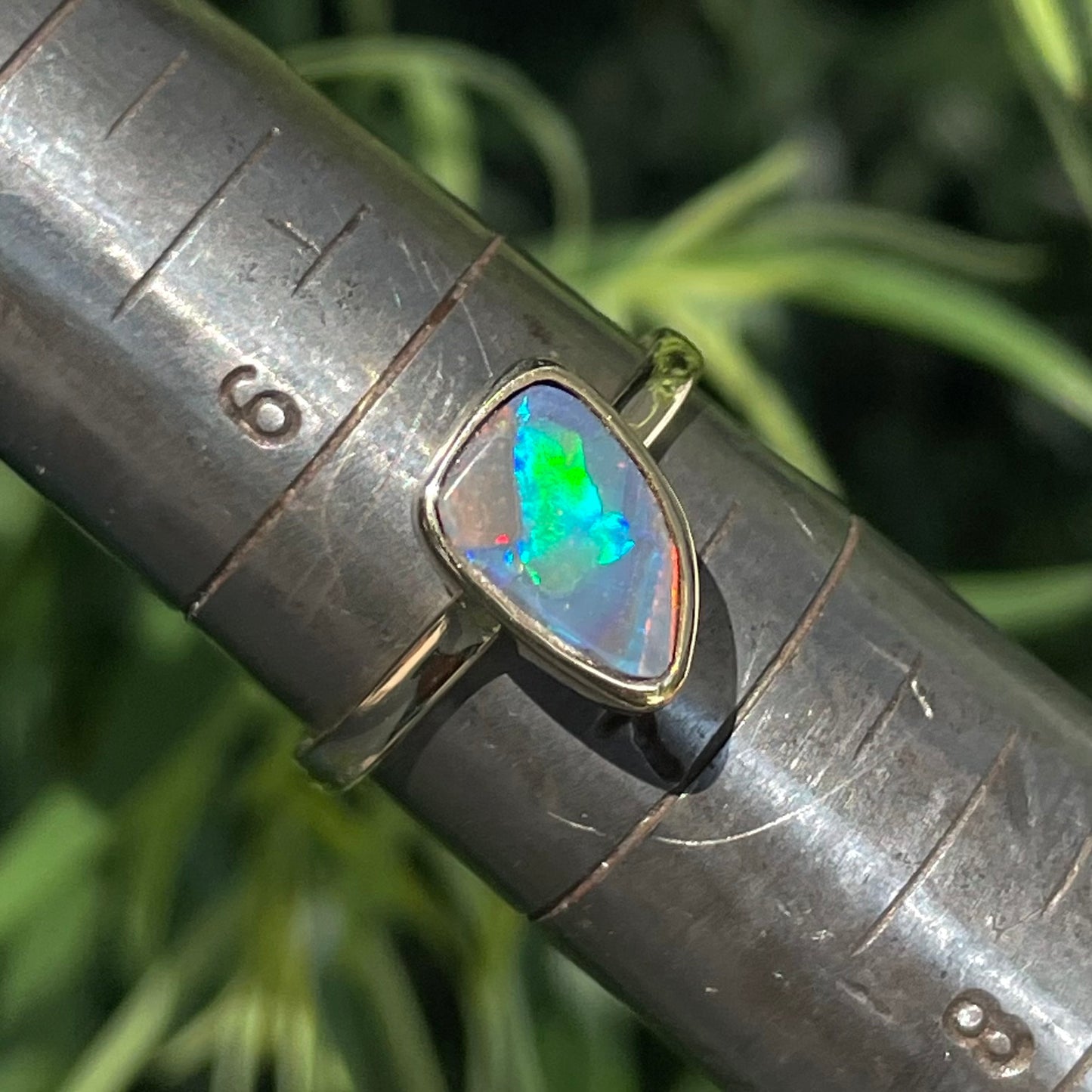 A handmade yellow gold solitaire ring bezel set with a Lightning Ridge red-on-black harlequin opal.