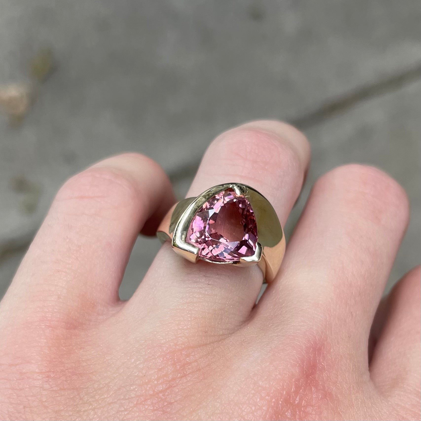A unisex trillion cut pink tourmaline ring half bezel set in 14k yellow gold.