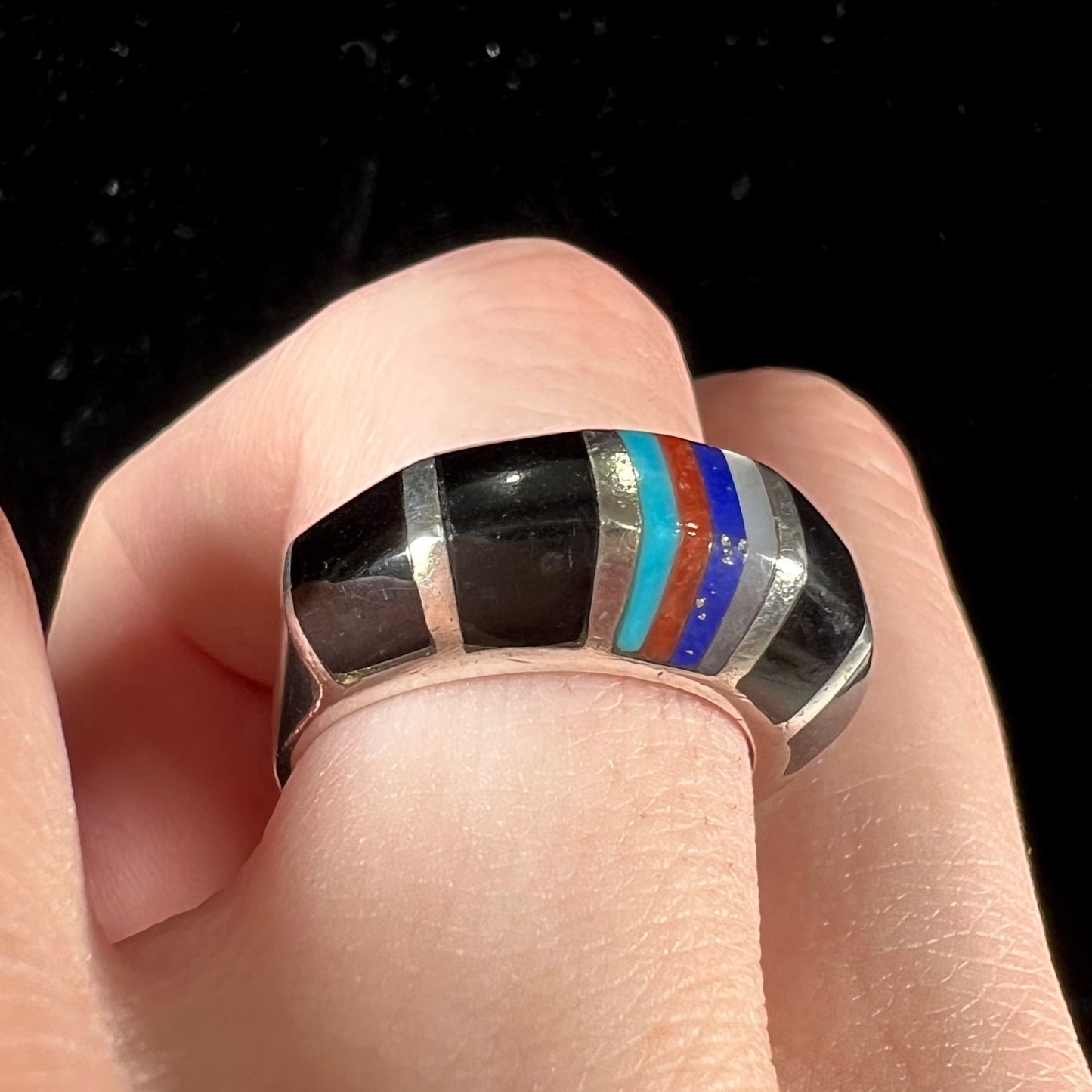 A sterling silver ring inlaid with onyx, turquoise, coral, lapis lazuli, and mother of pearl stones.
