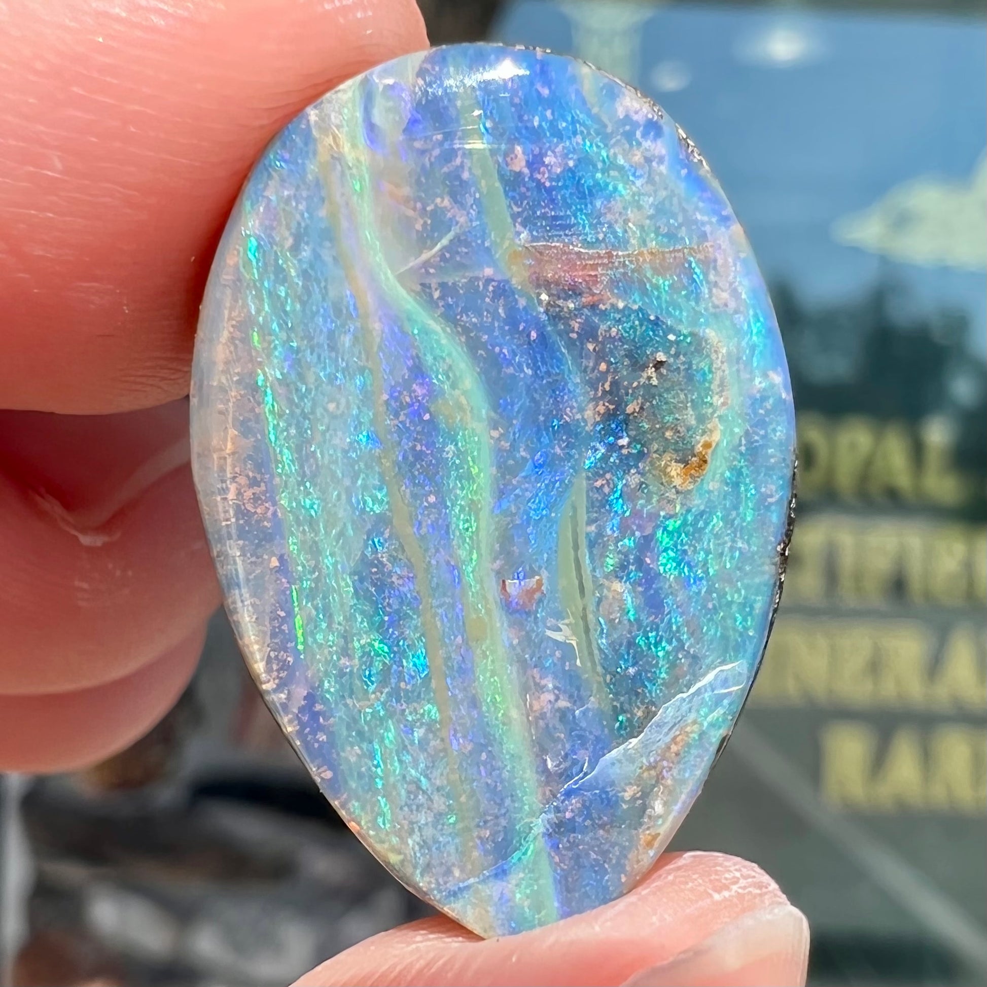 A loose, pear shaped Australian boulder opal stone.  The predominant colors are purple, green, and aqua.