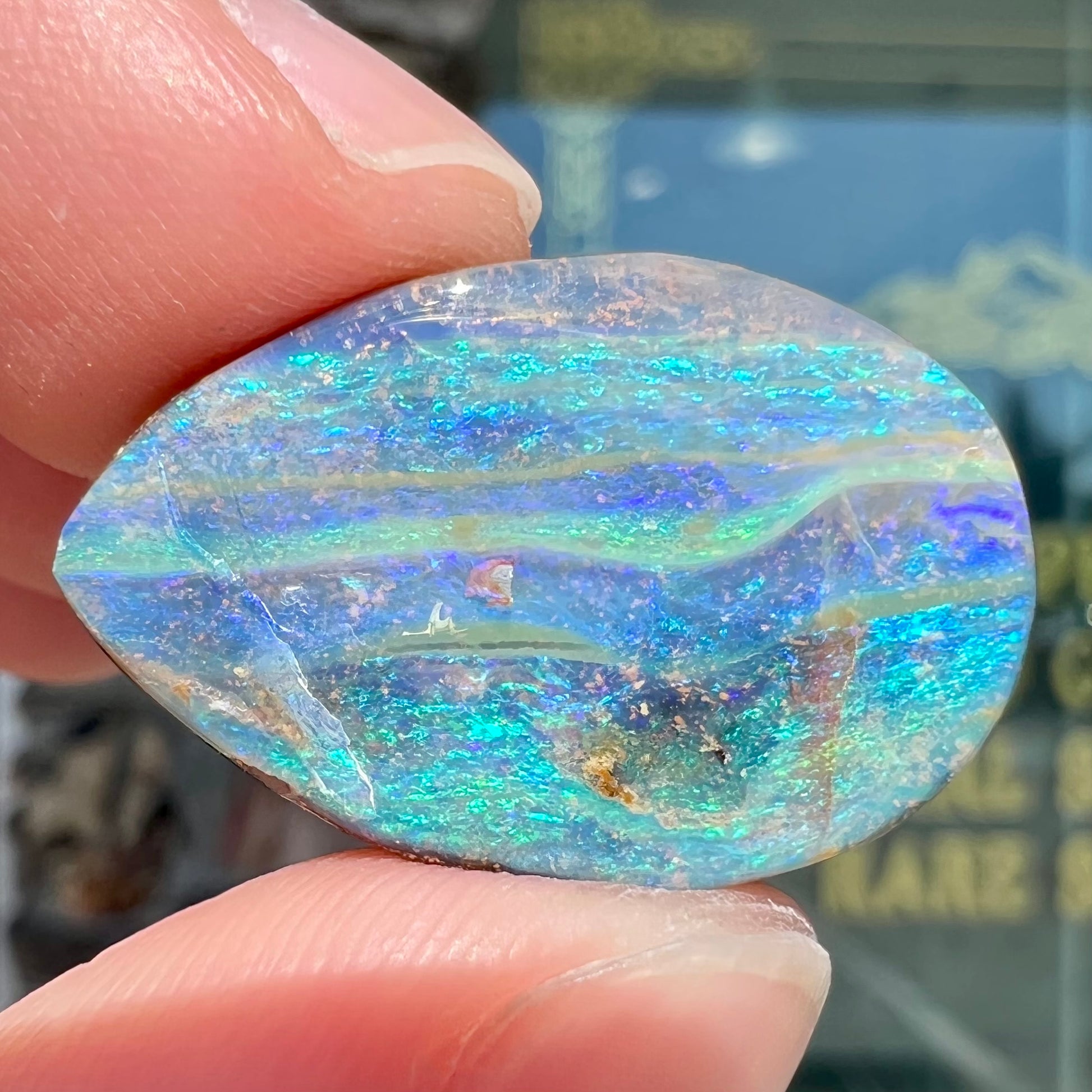 A loose, pear shaped Australian boulder opal stone.  The predominant colors are purple, green, and aqua.