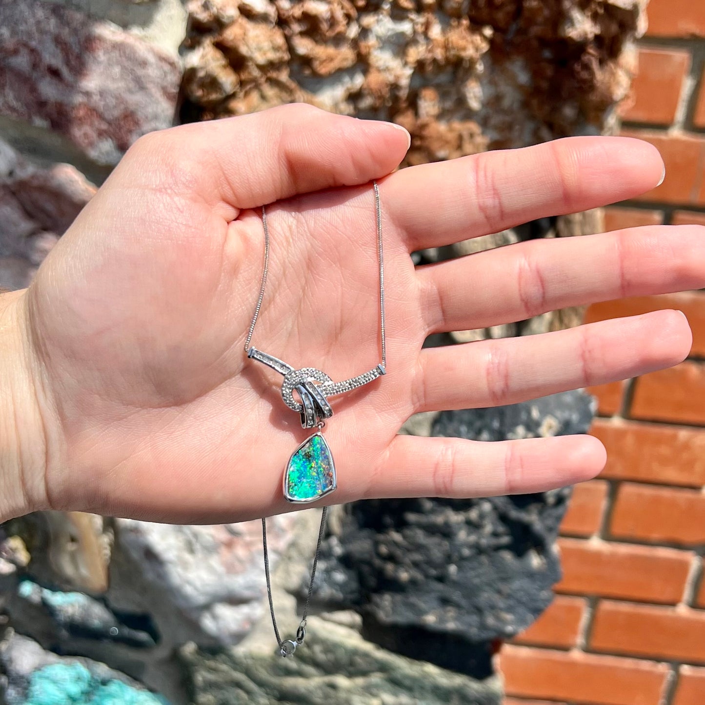 A white gold necklace set with diamonds and a dangling, bezel set boulder opal.