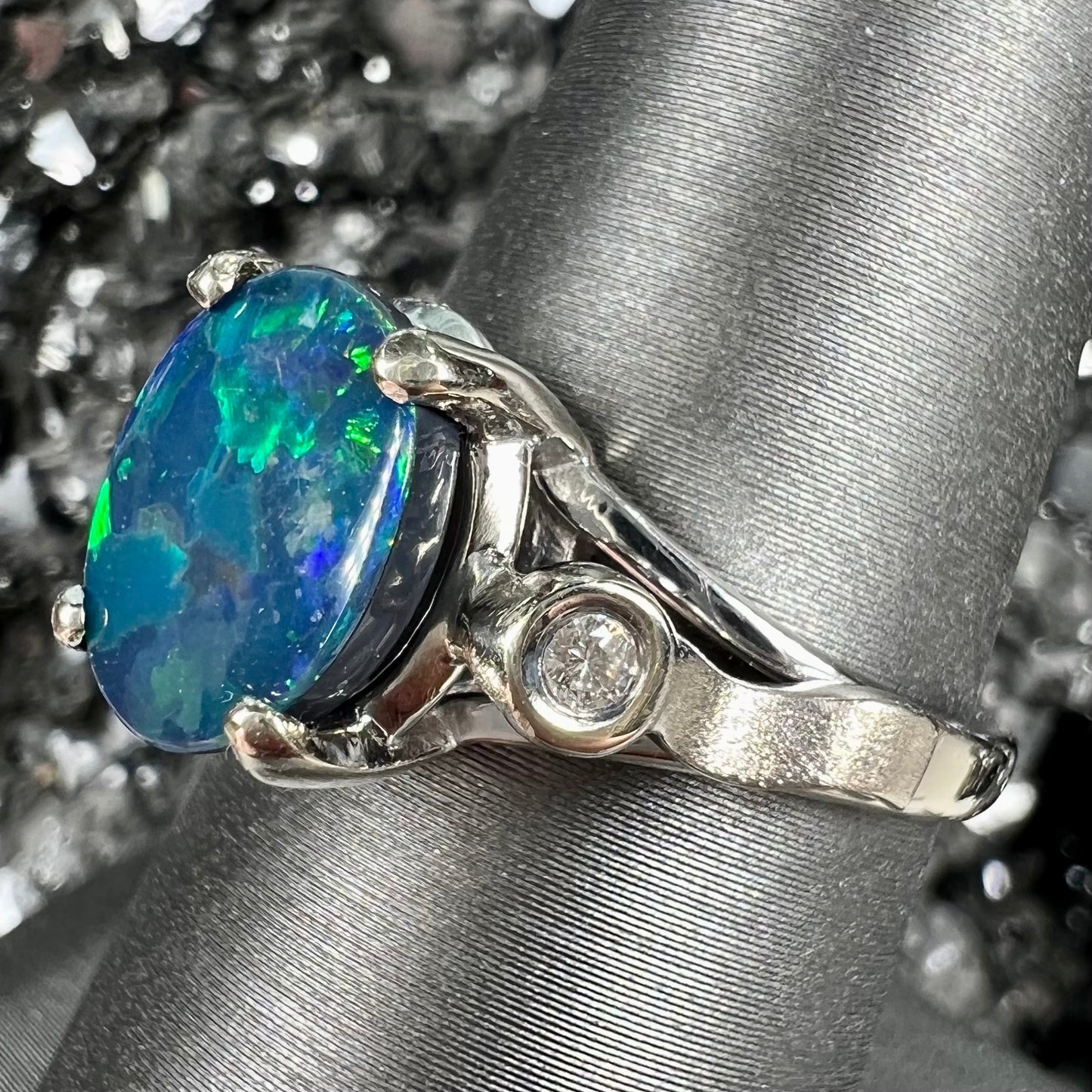 A white gold, oval cabochon cut black opal doublet ring set with two round diamond accent stones.