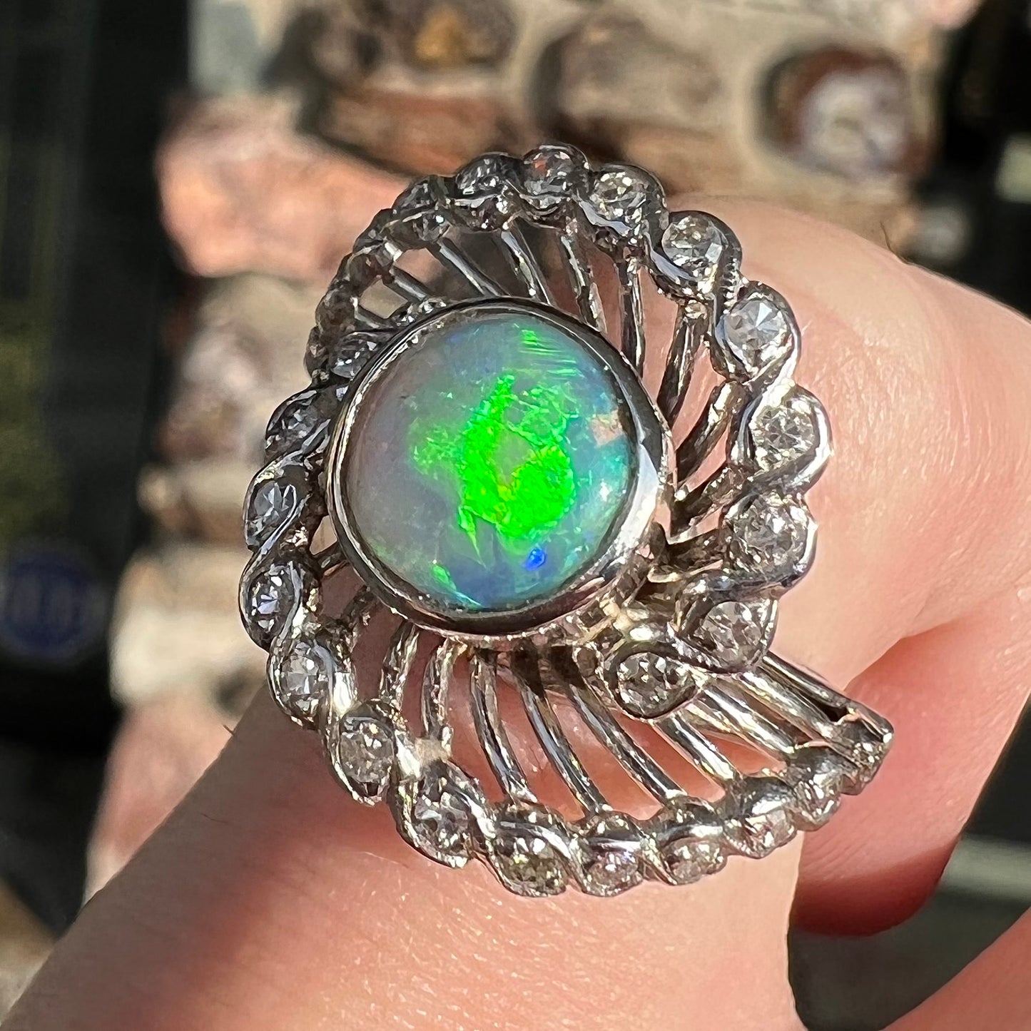 A white gold ring featuring a round cabochon cut black opal set in a swirl of round cut diamonds.