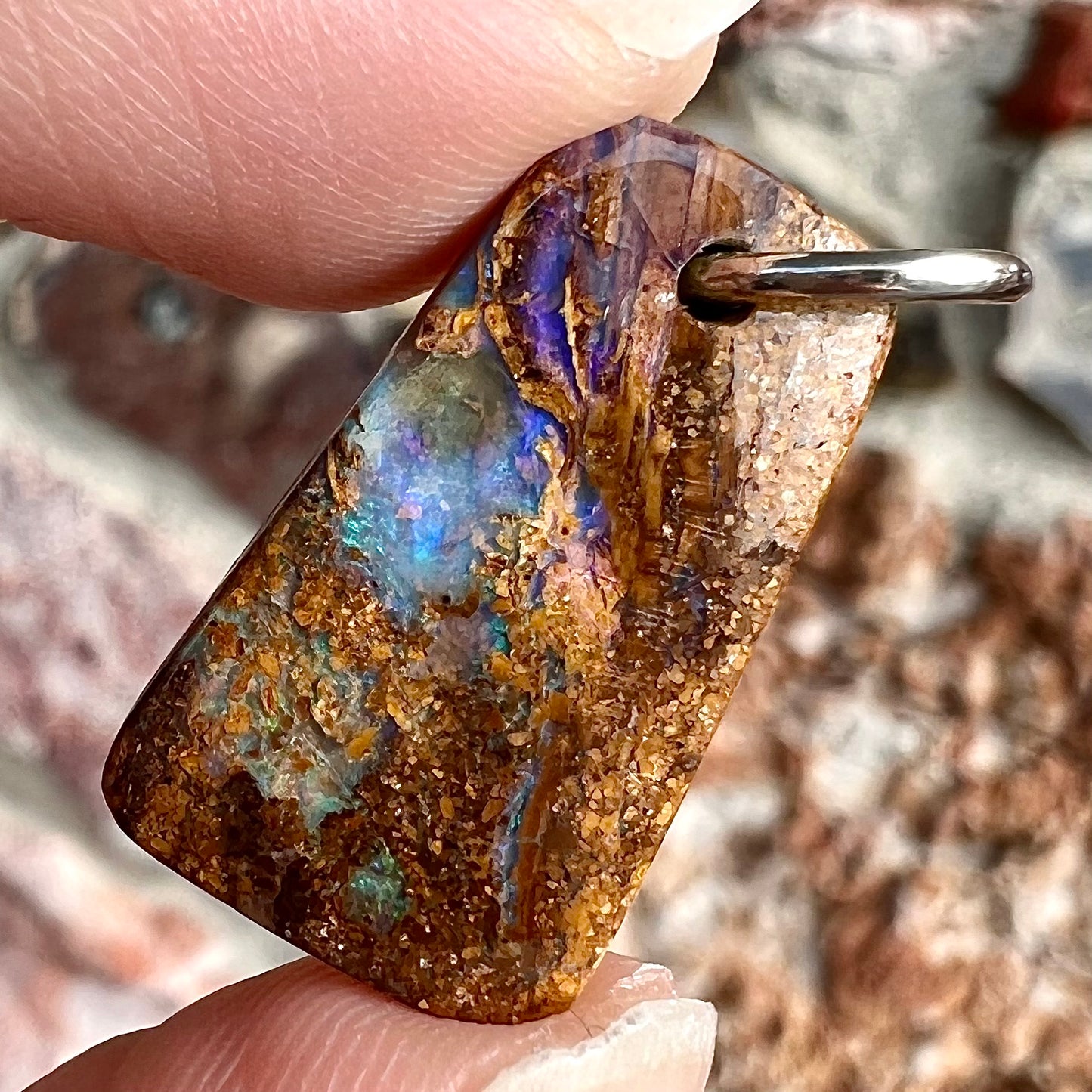 A drilled boulder opal stone with a sterling silver ring through the hole to be worn as a pendant.