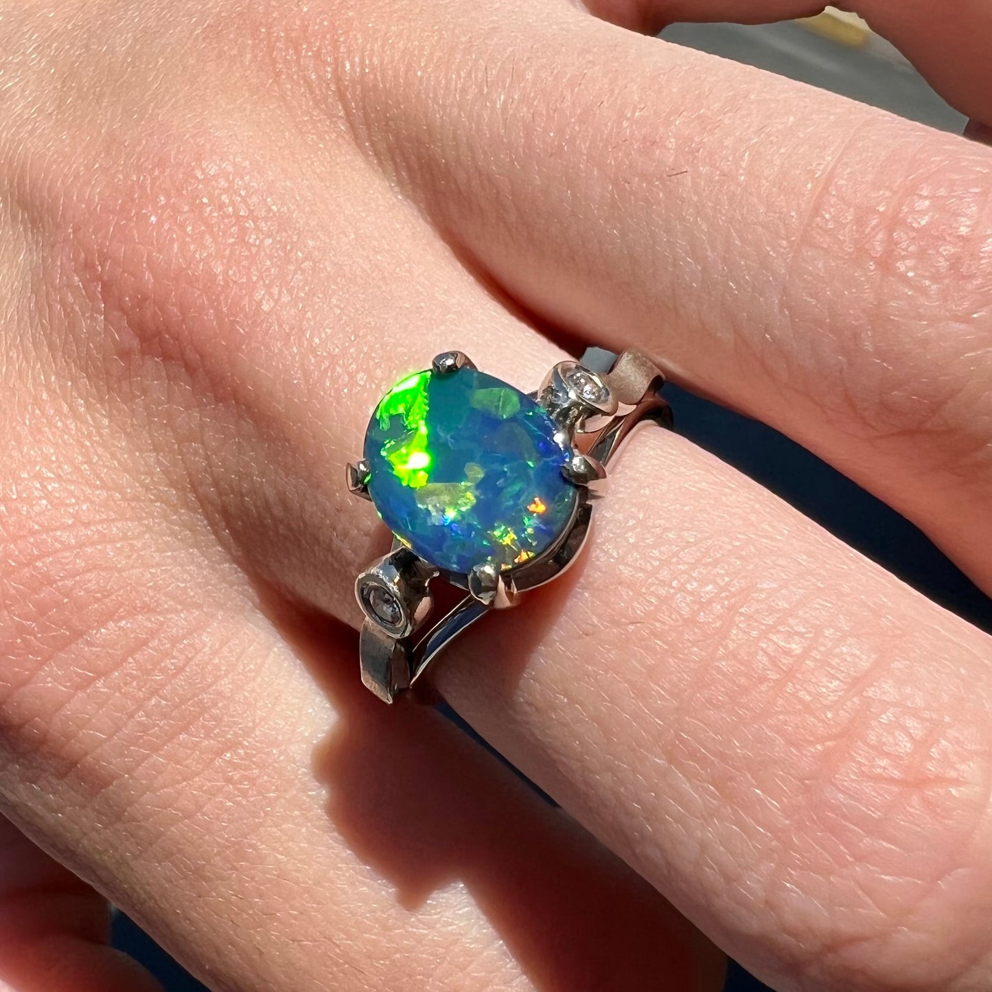 A white gold, oval cabochon cut black opal doublet ring set with two round diamond accent stones.