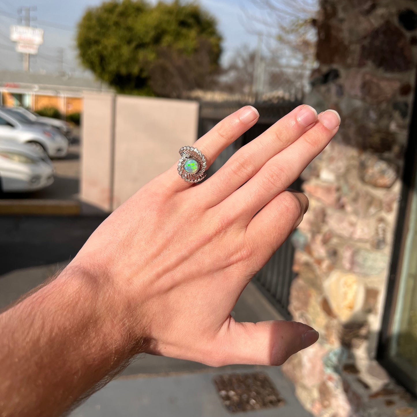 A white gold ring featuring a round cabochon cut black opal set in a swirl of round cut diamonds.