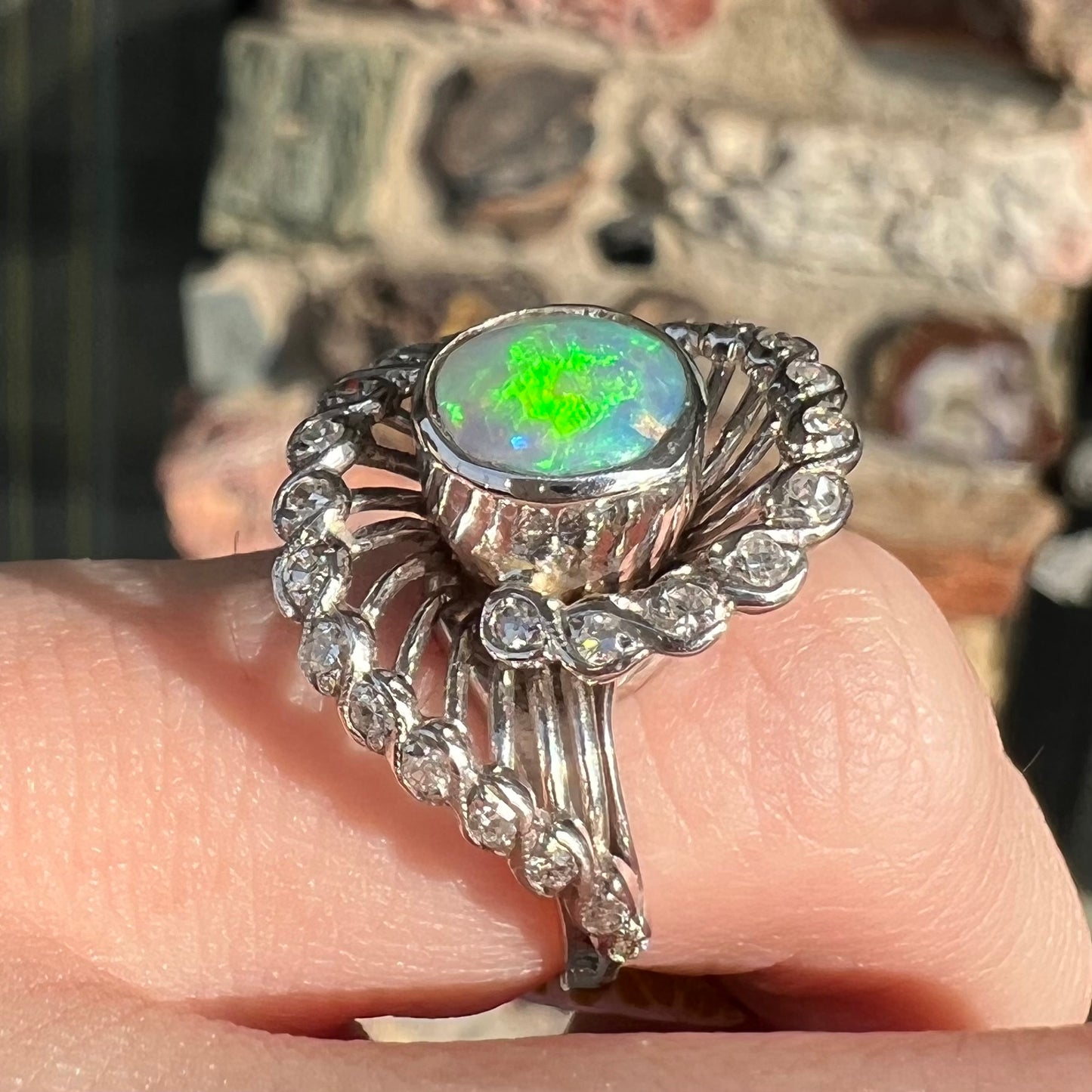 A white gold ring featuring a round cabochon cut black opal set in a swirl of round cut diamonds.