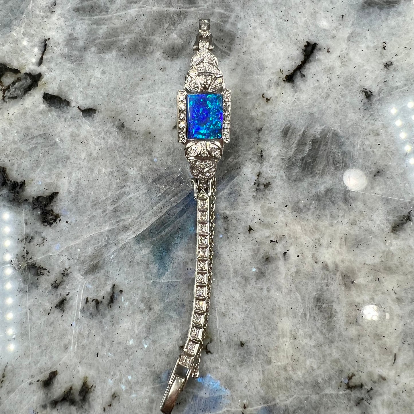 A vintage, art deco style white gold and diamond bracelet set with a rectangular shape black boulder opal stone.
