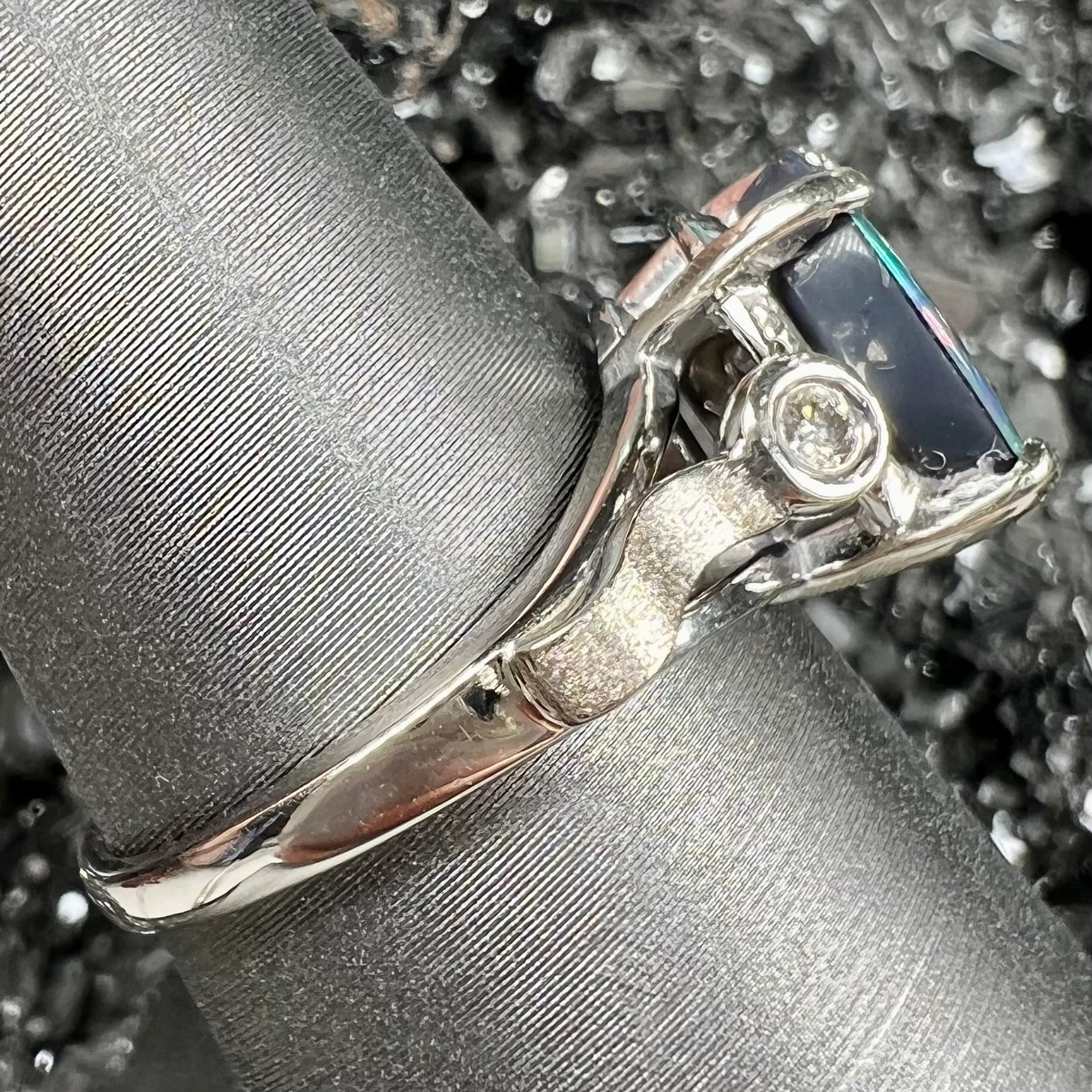 A white gold, oval cabochon cut black opal doublet ring set with two round diamond accent stones.