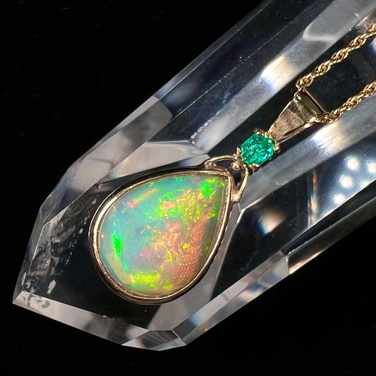 A yellow gold bezel set Ethiopian fire opal drop pendant.  There is an emerald set in the bail.