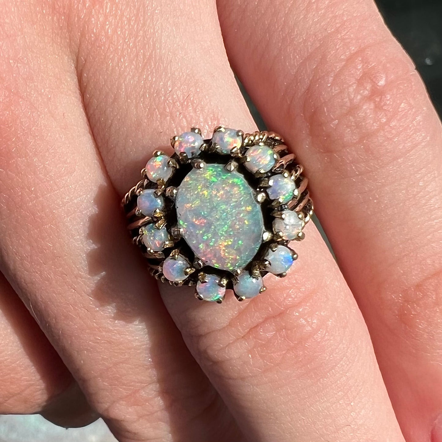 Vintage yellow gold oval opal cabochon ring set with 12 round opals in a halo around the center stone.