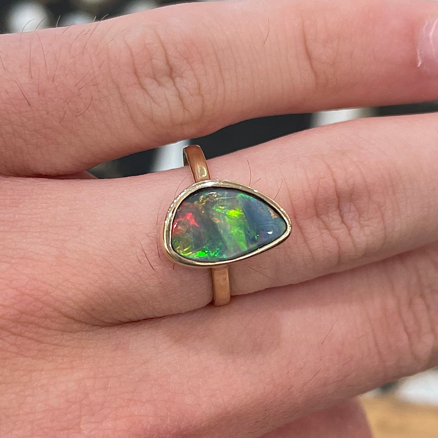 A freeform cut semi-black opal from Lightning Ridge, Australia set in a bezel set yellow gold solitaire ring.
