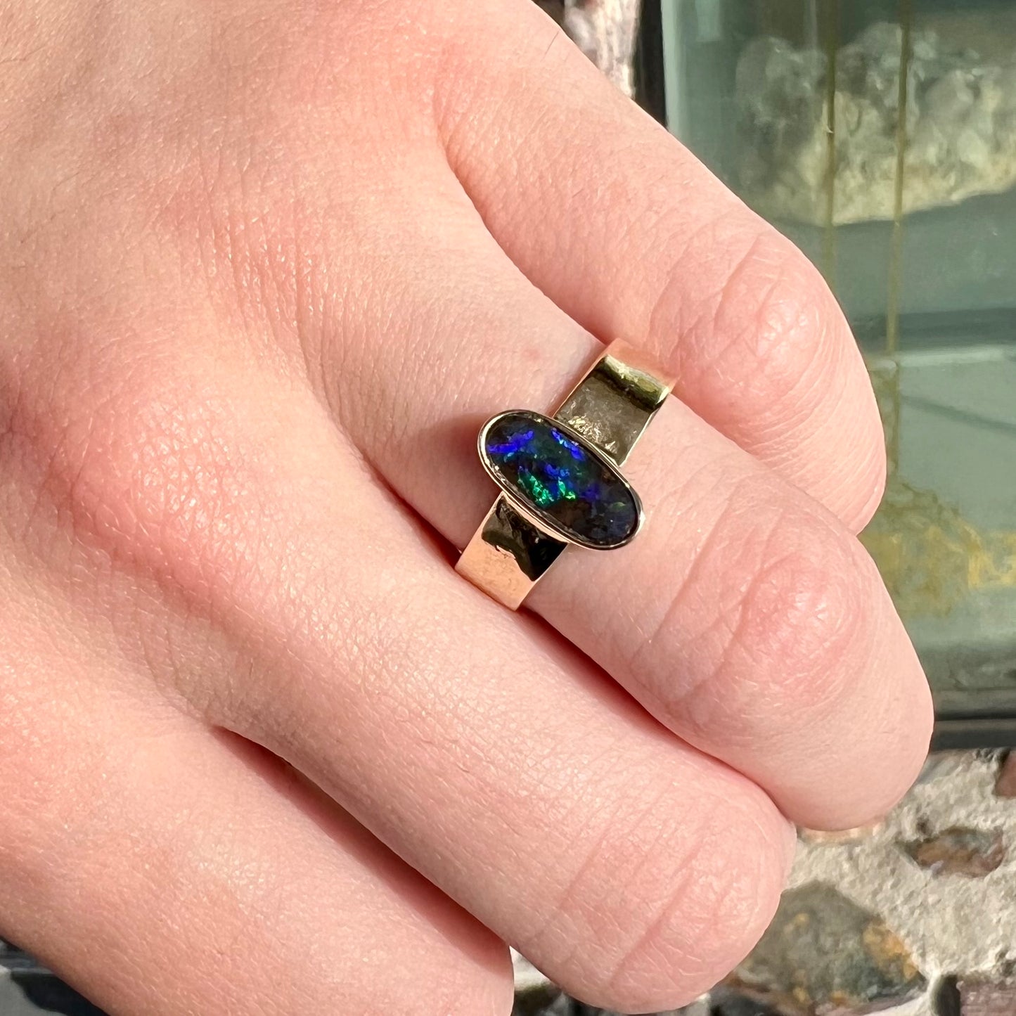A blue green oval cabochon cut Australian boulder opal set in a yellow gold solitaire ring.