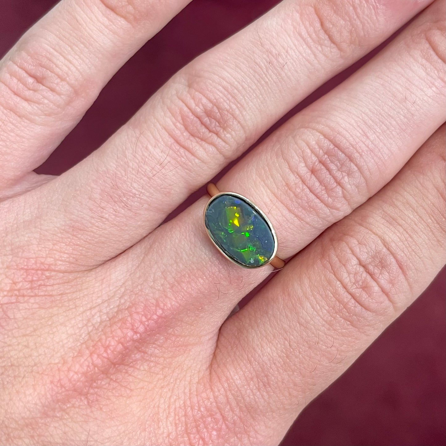 A handmade Lightning Ridge black opal solitaire ring in yellow gold. Fire is green.
