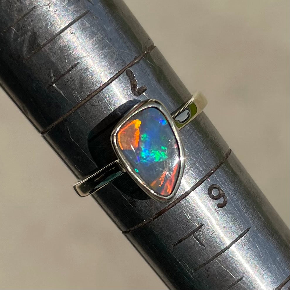 A handmade yellow gold solitaire ring bezel set with a Lightning Ridge red-on-black harlequin opal.