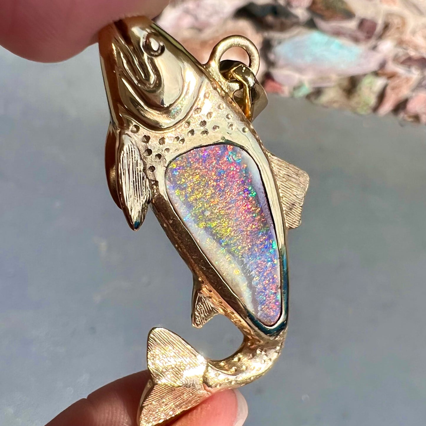 A yellow gold fish pendant detailed to look like a rainbow trout. The body of the fish is set with a color changing black opal stone.