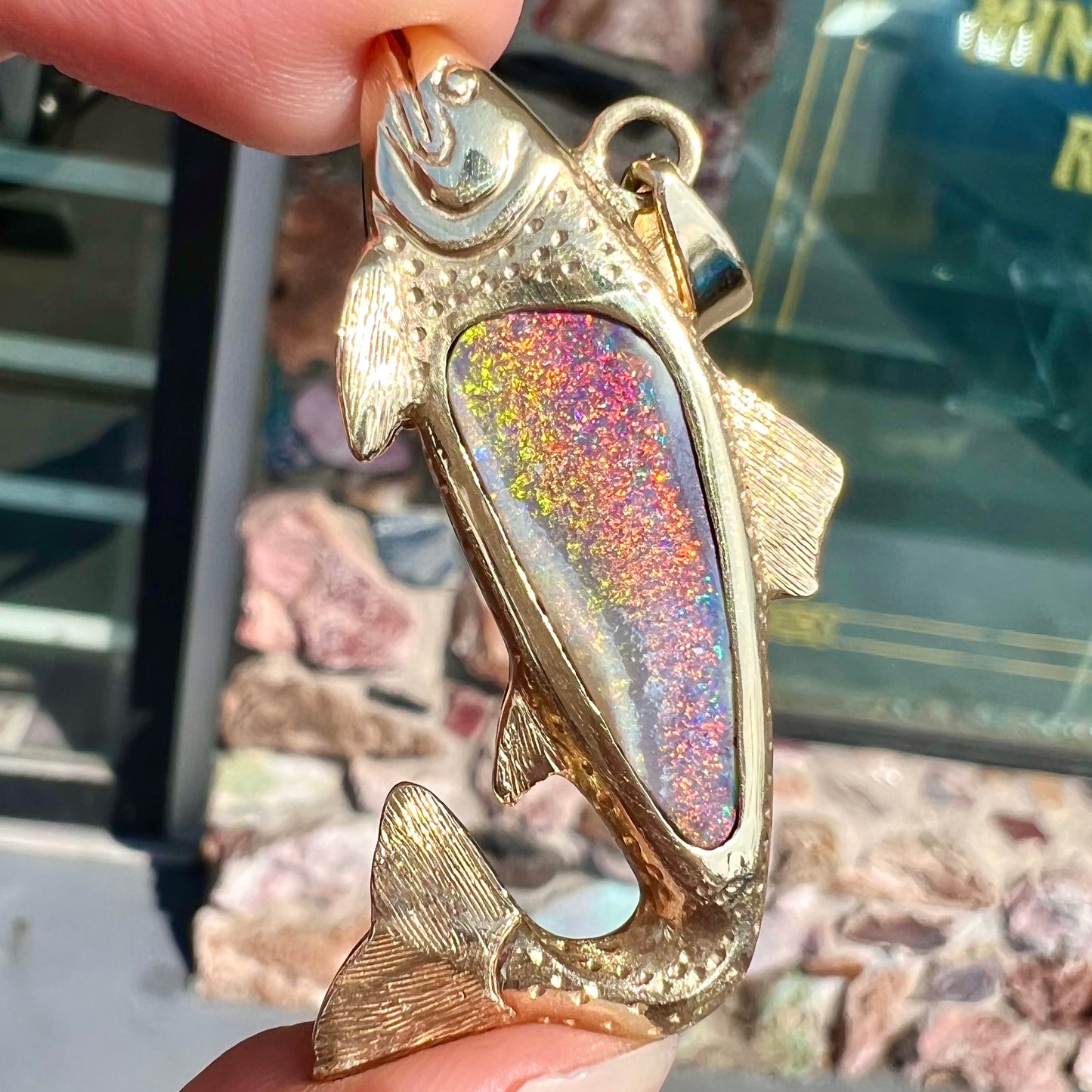 A yellow gold fish pendant detailed to look like a rainbow trout. The body of the fish is set with a color changing black opal stone.