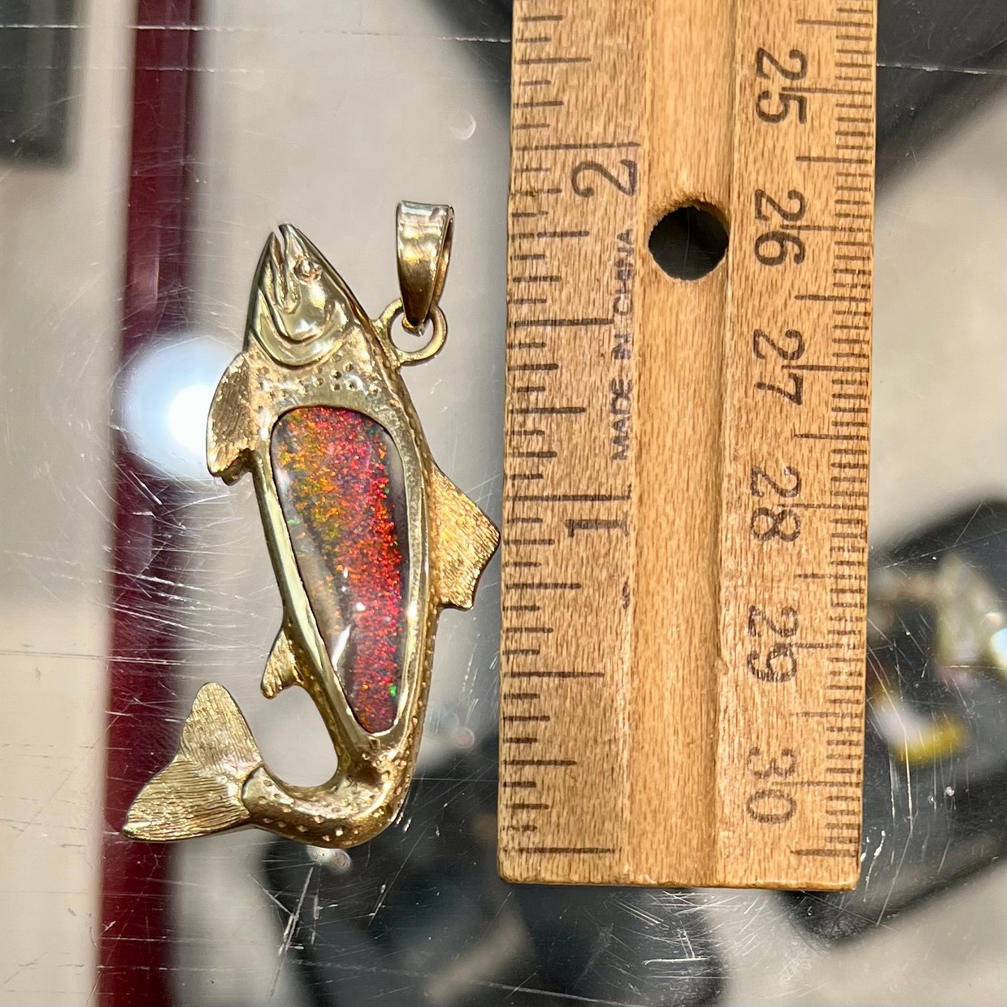A yellow gold fish pendant detailed to look like a rainbow trout. The body of the fish is set with a color changing black opal stone.