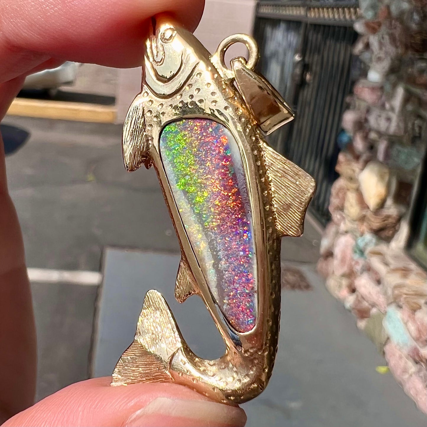 A yellow gold fish pendant detailed to look like a rainbow trout. The body of the fish is set with a color changing black opal stone.