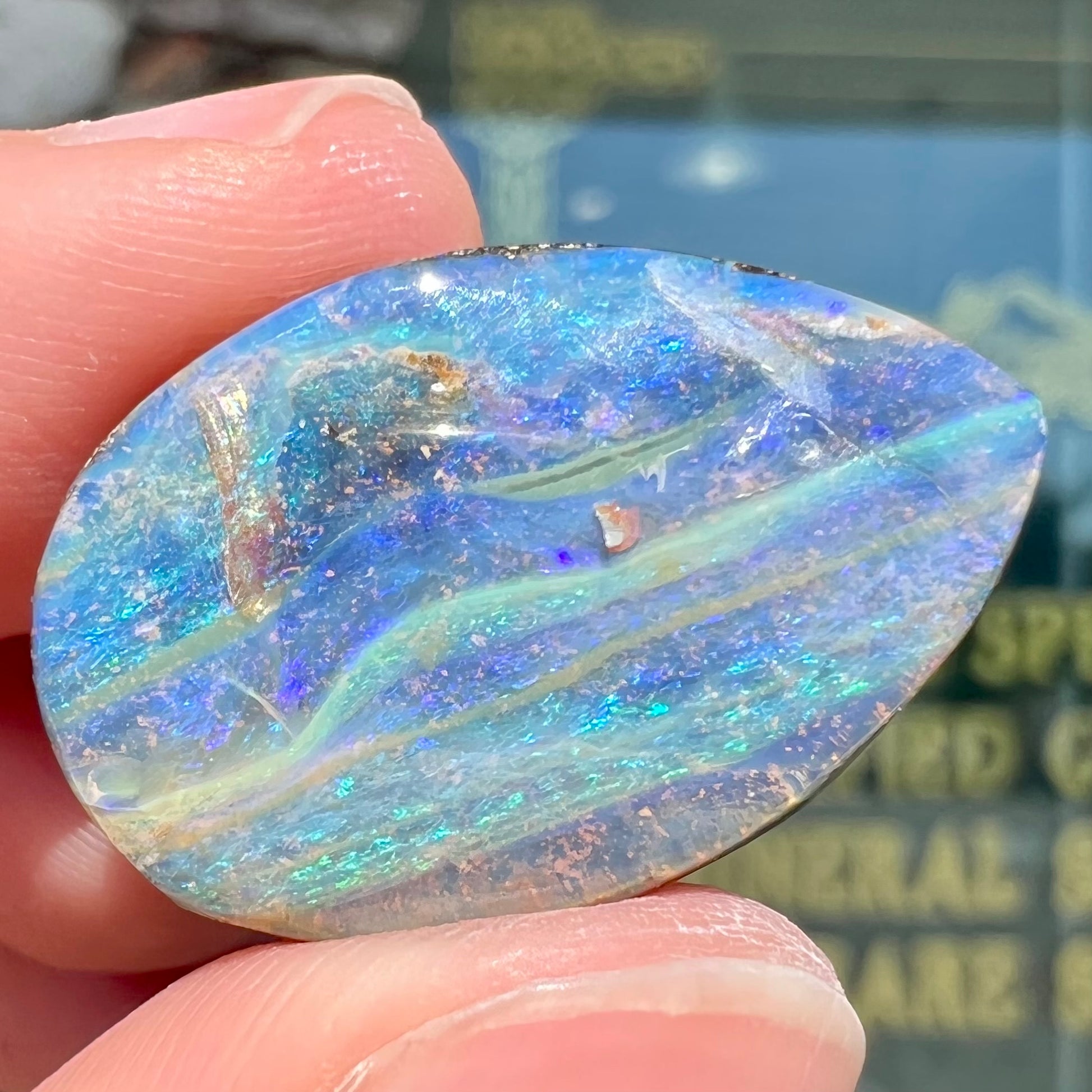 A loose, pear shaped Australian boulder opal stone.  The predominant colors are purple, green, and aqua.
