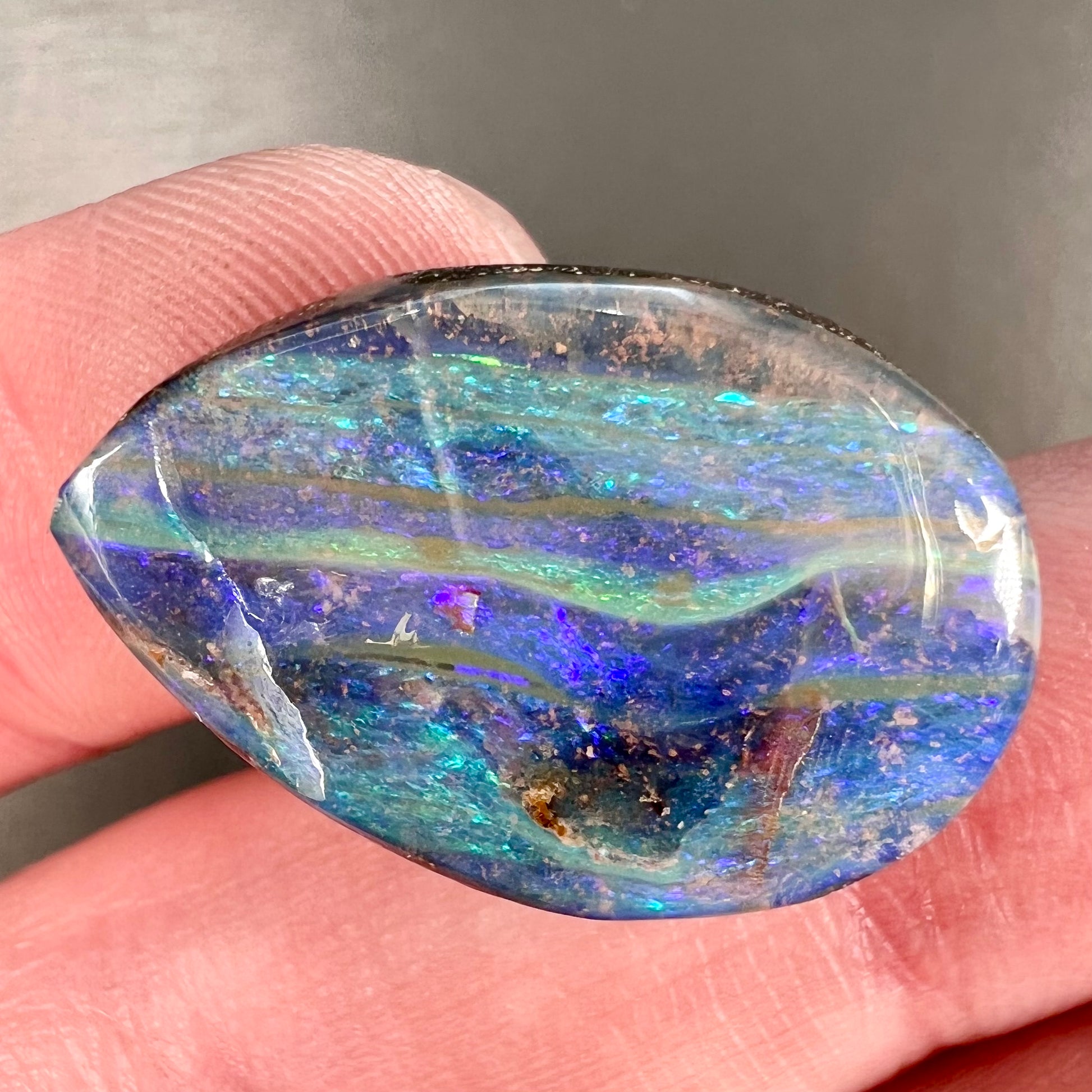 A loose, pear shaped Australian boulder opal stone.  The predominant colors are purple, green, and aqua.