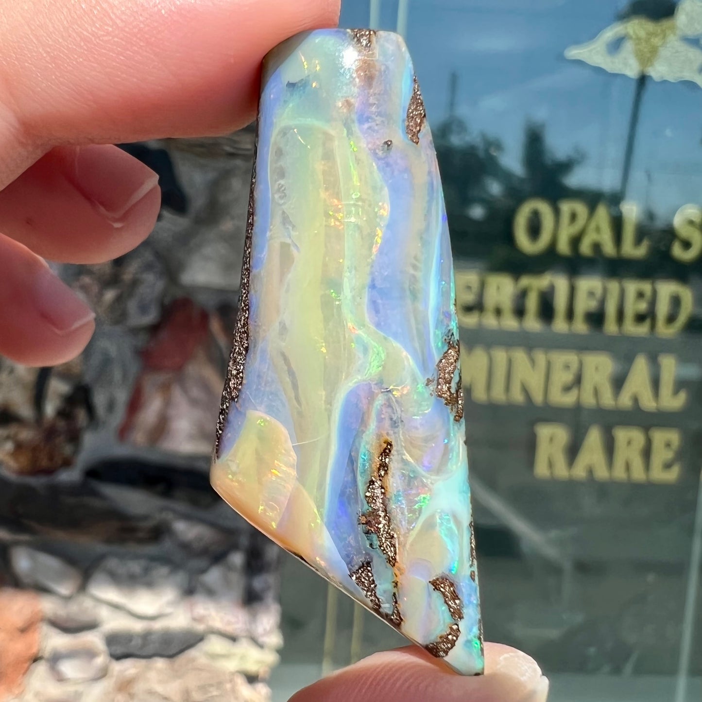 A freeform shaped, polished boulder opal stone from Queensland, Australia. The stone has red, orange, green, and blue fire.