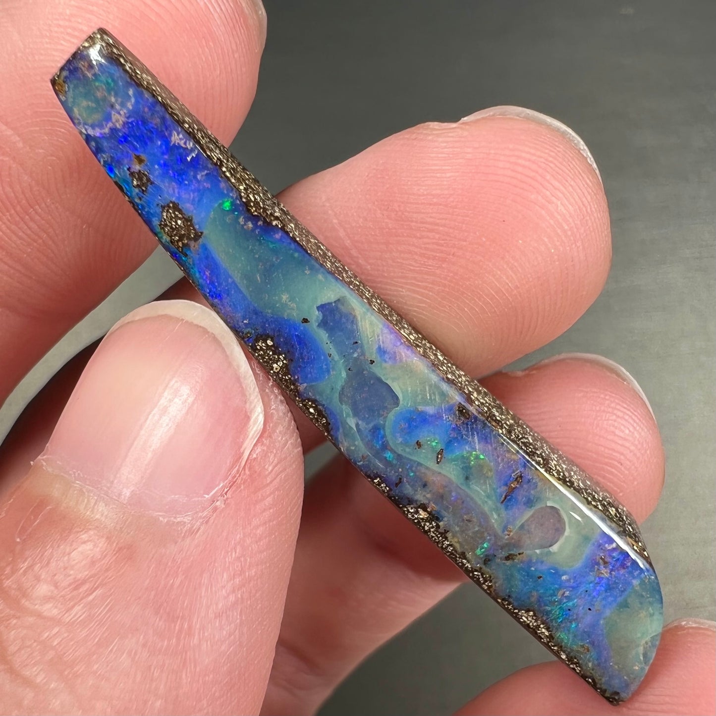 A loose, polished Quilpie boulder opal stone from Australia. The stone is predominantly blue.