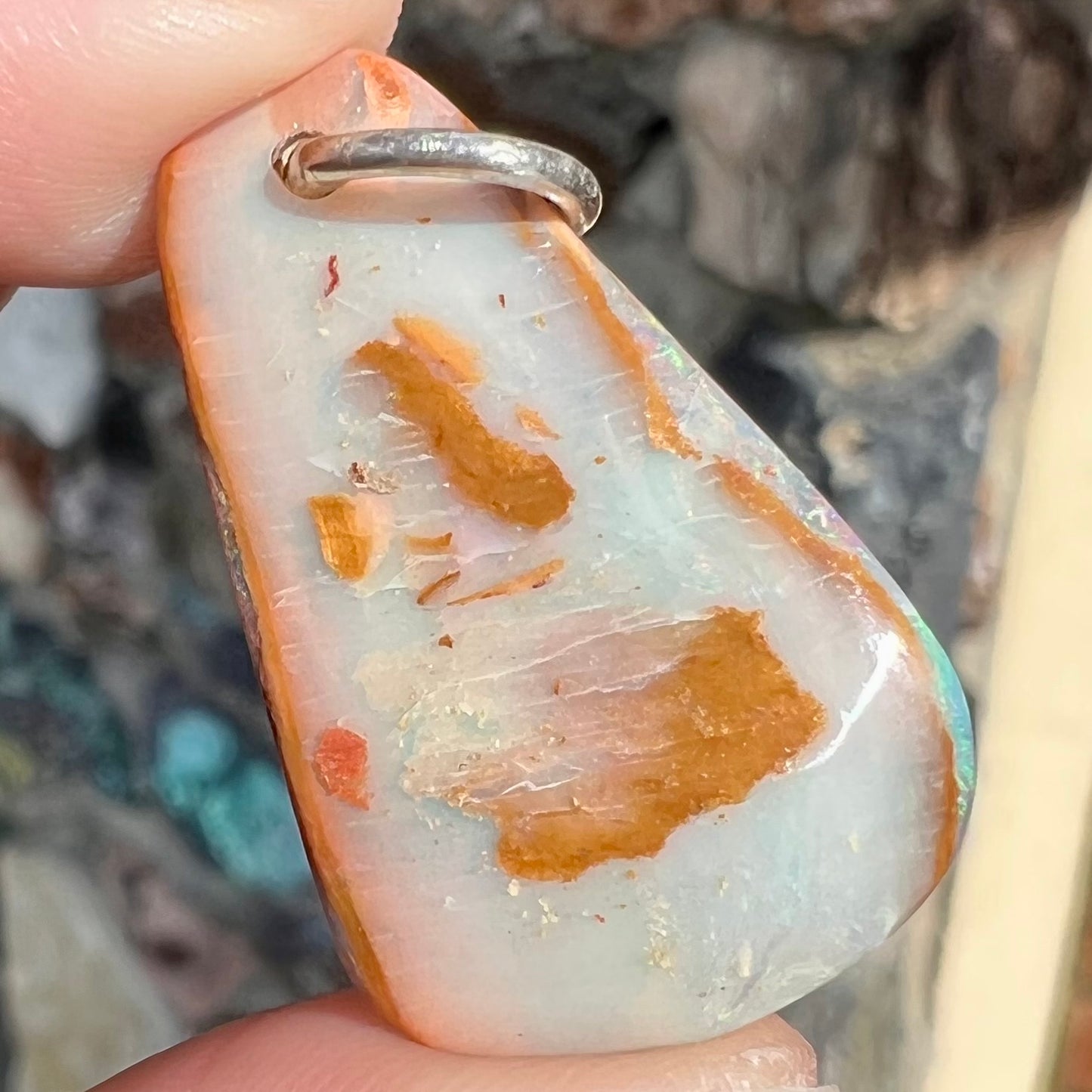 A drilled boulder opal stone with a sterling silver ring through the hole to be worn as a pendant.