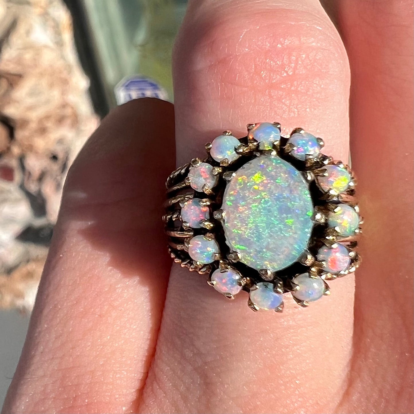 Vintage yellow gold oval opal cabochon ring set with 12 round opals in a halo around the center stone.
