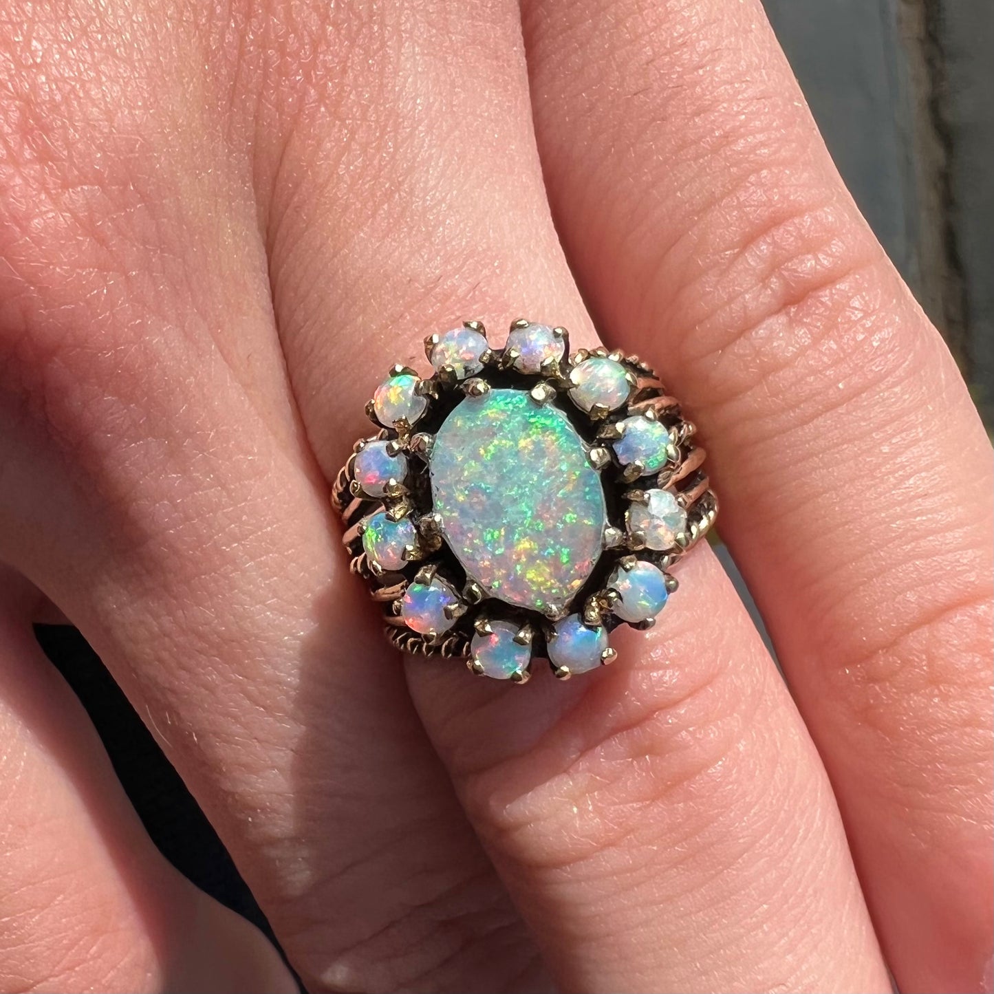 Vintage yellow gold oval opal cabochon ring set with 12 round opals in a halo around the center stone.
