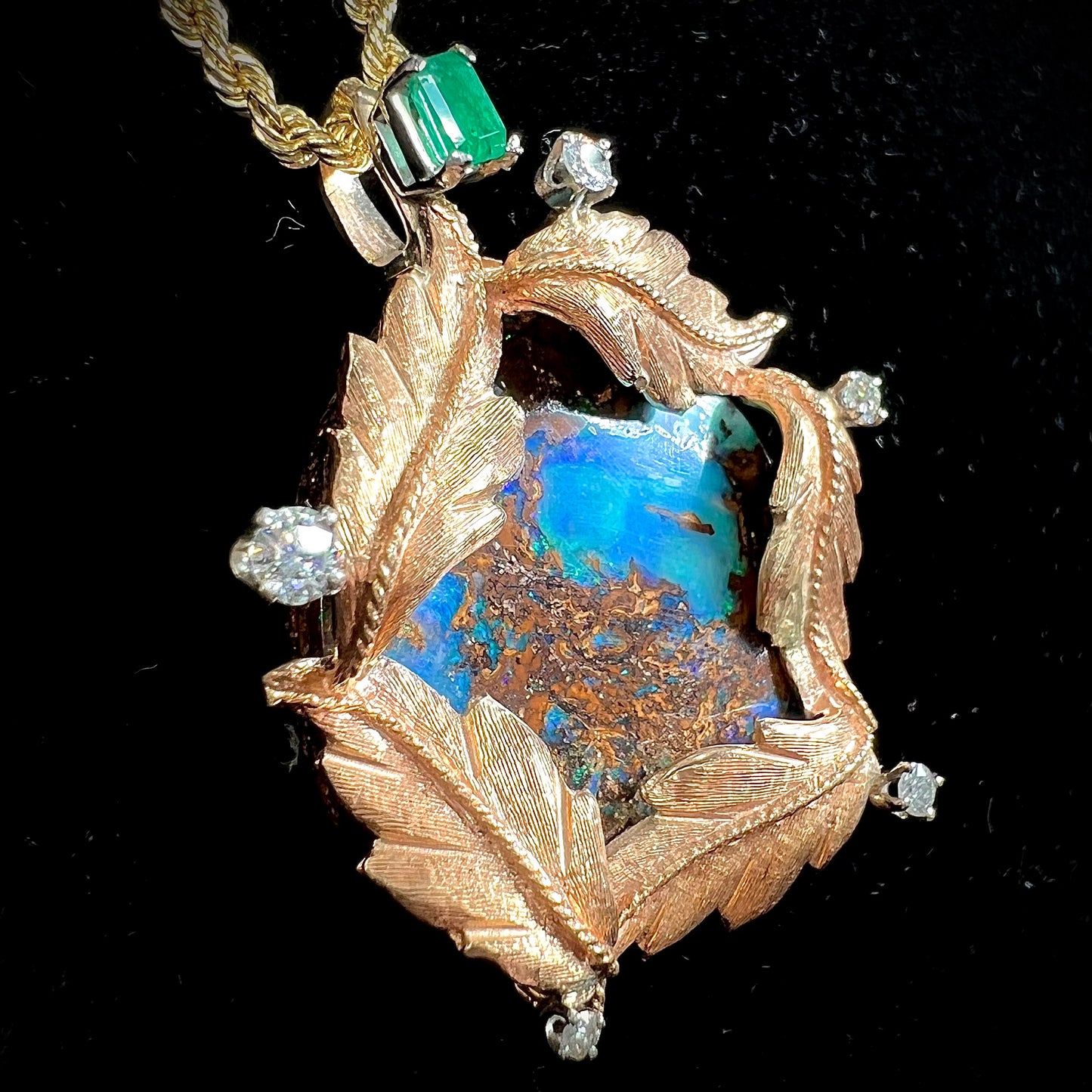 A gold opalized wood, diamond, and emerald pendant. The opal is set in a wreath of gold feathers that form a star.