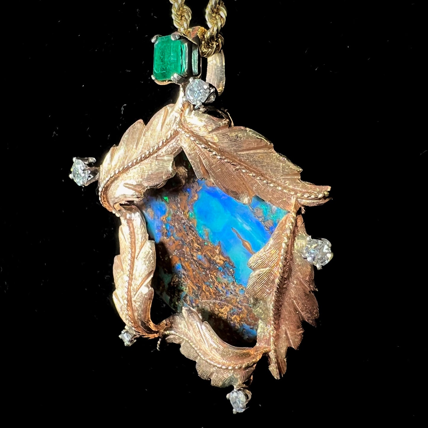 A gold opalized wood, diamond, and emerald pendant. The opal is set in a wreath of gold feathers that form a star.