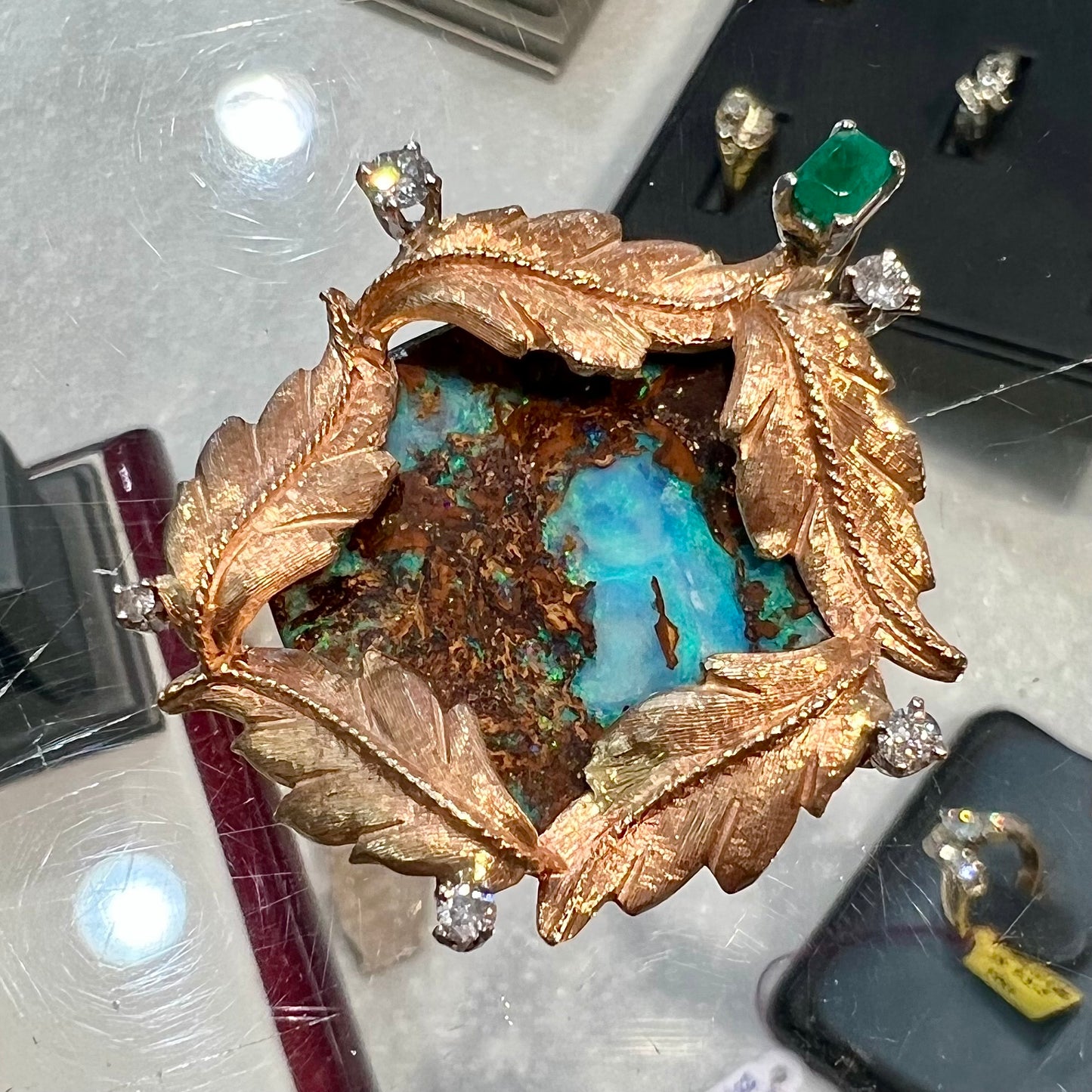 A gold opalized wood, diamond, and emerald pendant. The opal is set in a wreath of gold feathers that form a star.