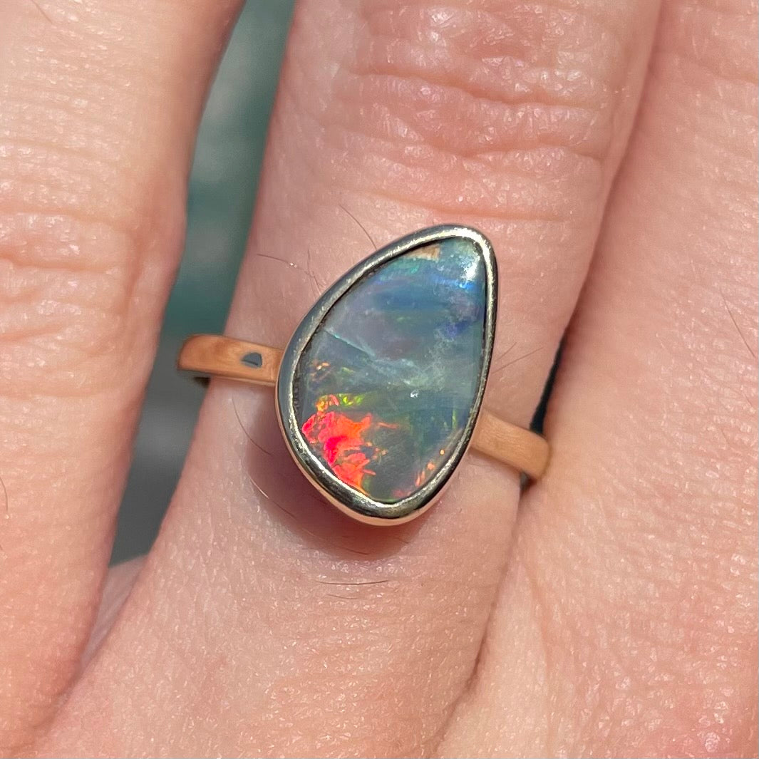 A freeform cut semi-black opal from Lightning Ridge, Australia set in a bezel set yellow gold solitaire ring.