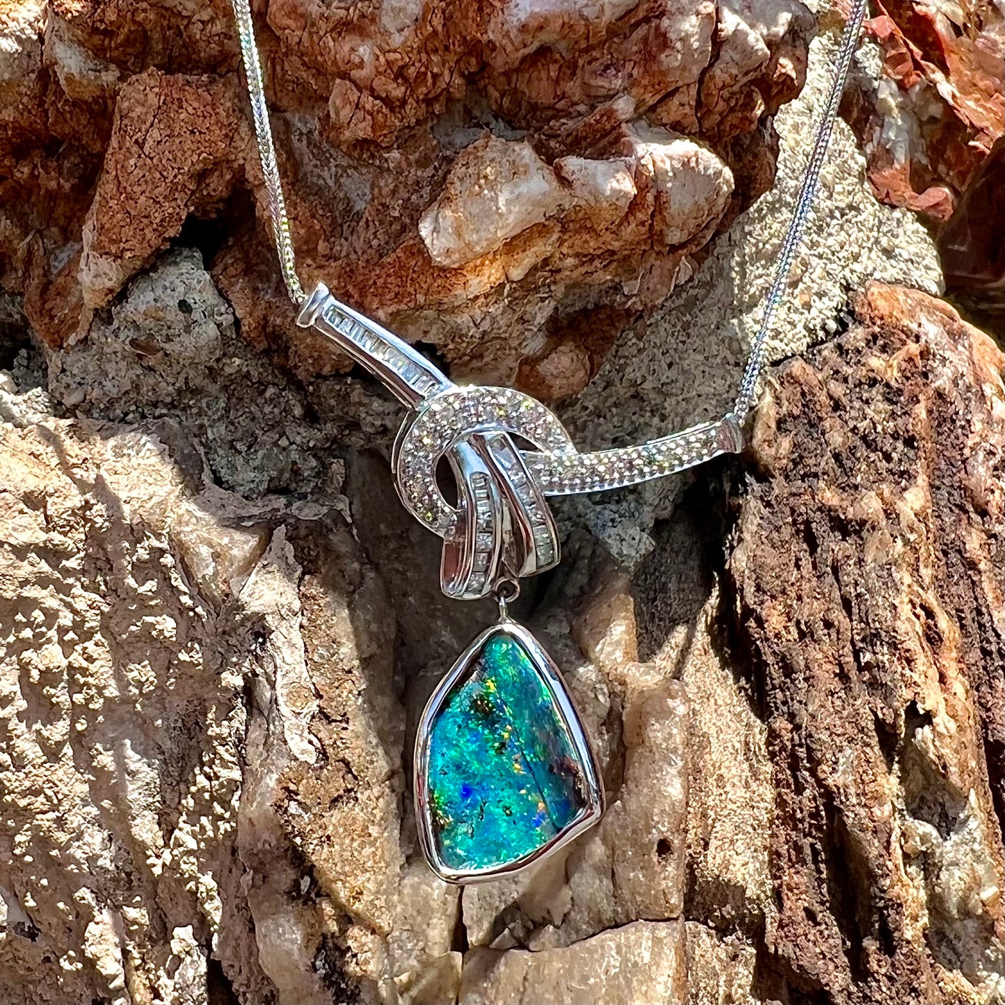 A white gold necklace set with diamonds and a dangling, bezel set boulder opal.