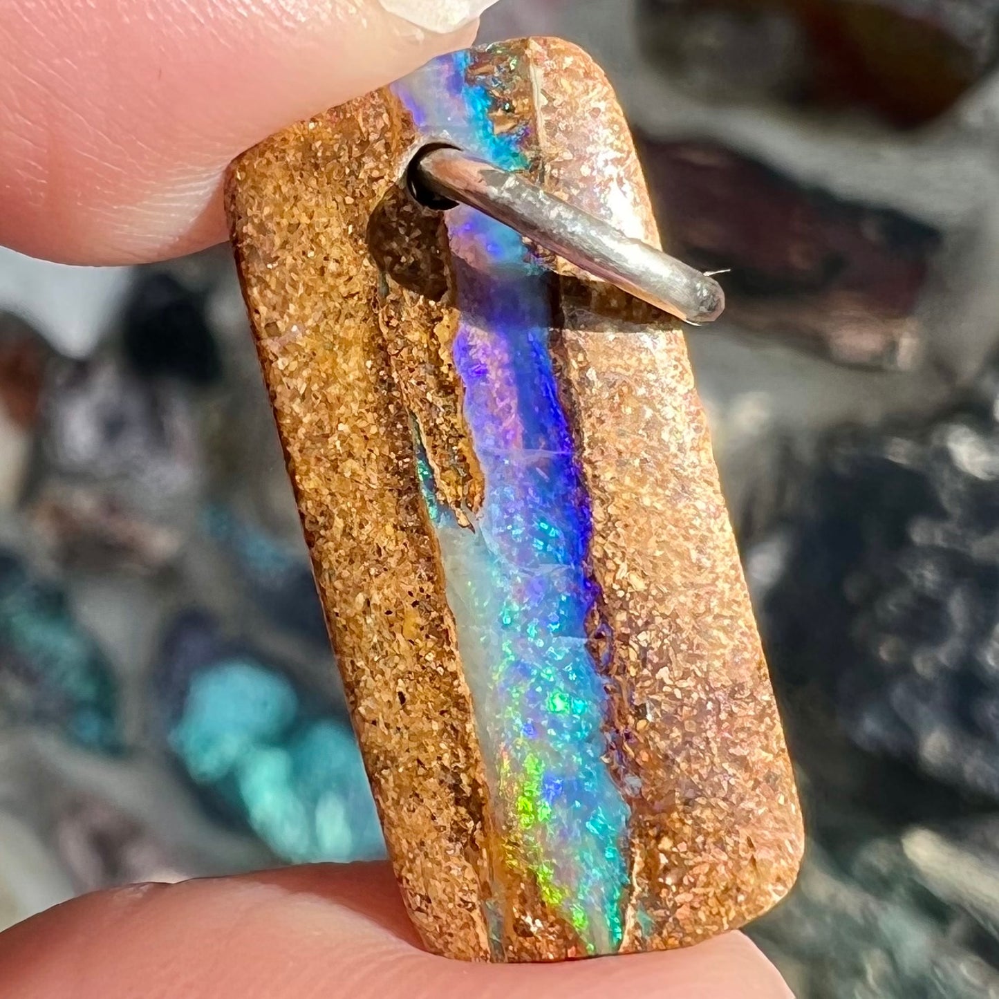 A drilled boulder opal stone with a sterling silver ring through the hole to be worn as a pendant.