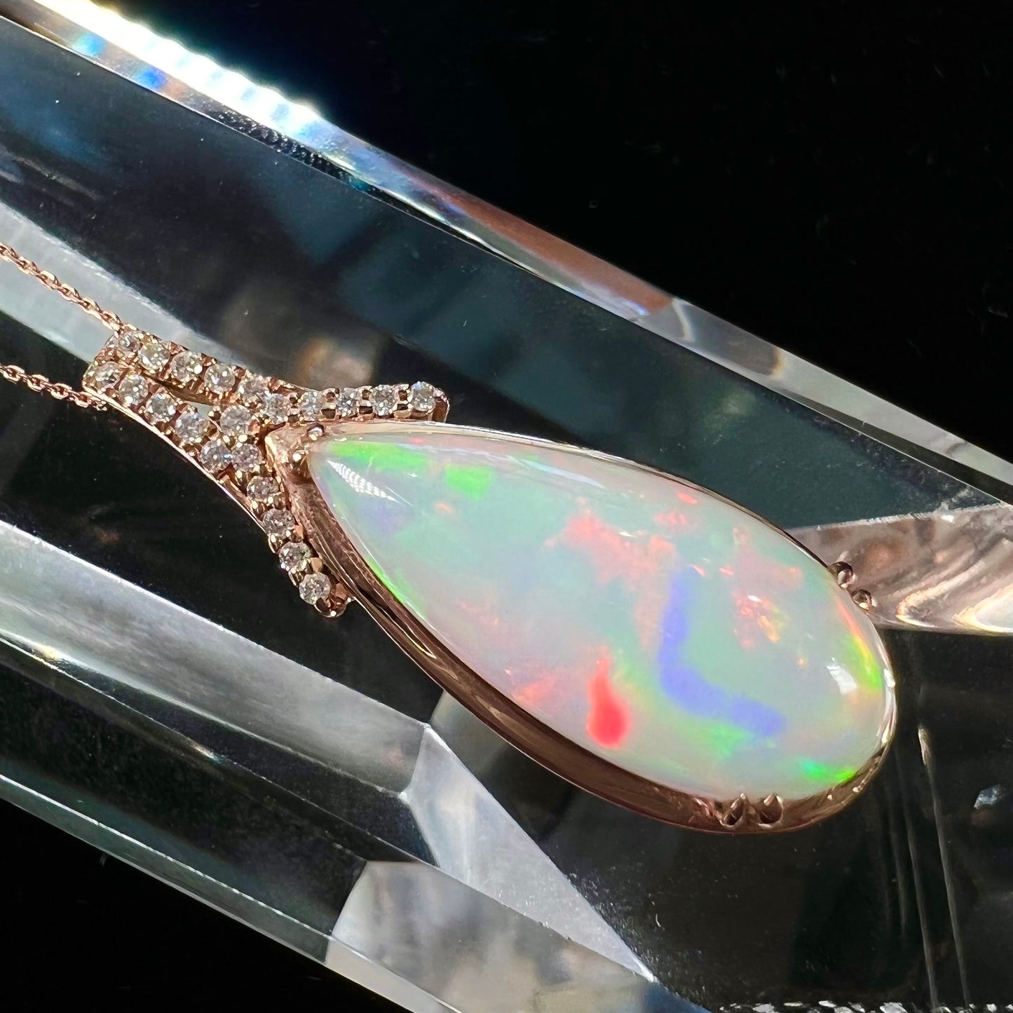 A rose gold, teardrop shaped fire opal and diamond necklace on a cable chain.