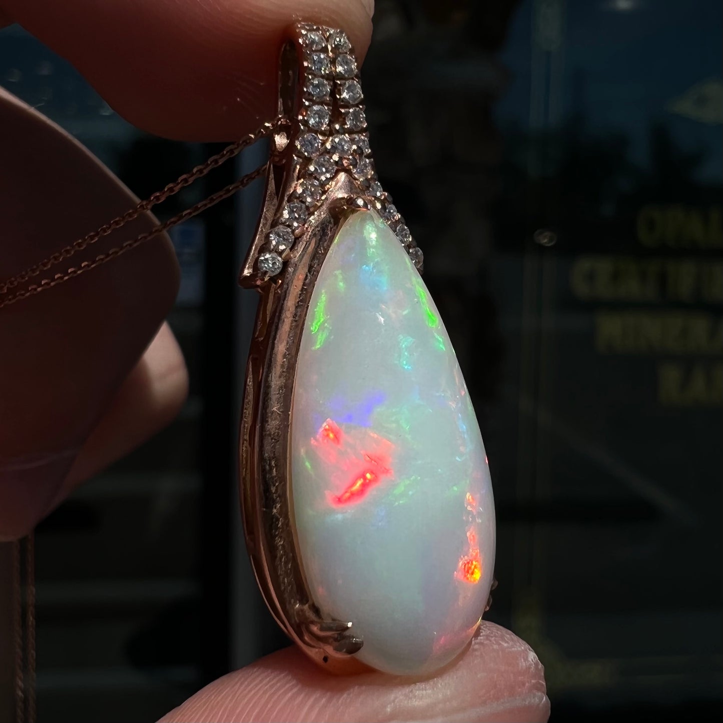 A rose gold, teardrop shaped fire opal and diamond necklace on a cable chain.