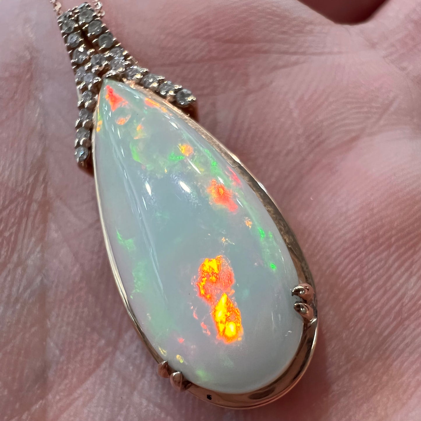 A rose gold, teardrop shaped fire opal and diamond necklace on a cable chain.