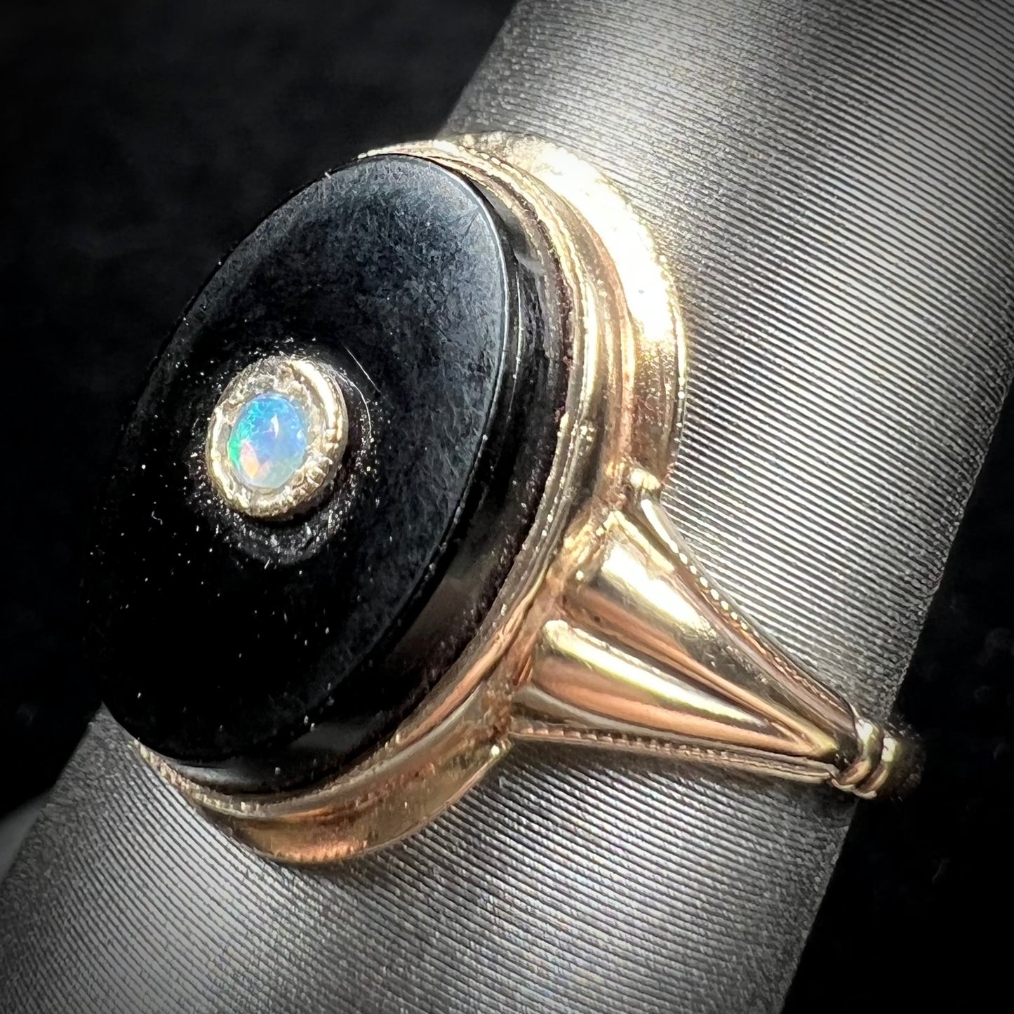 A yellow gold onyx ring set with a round cabochon cut opal bezel set into the onyx.