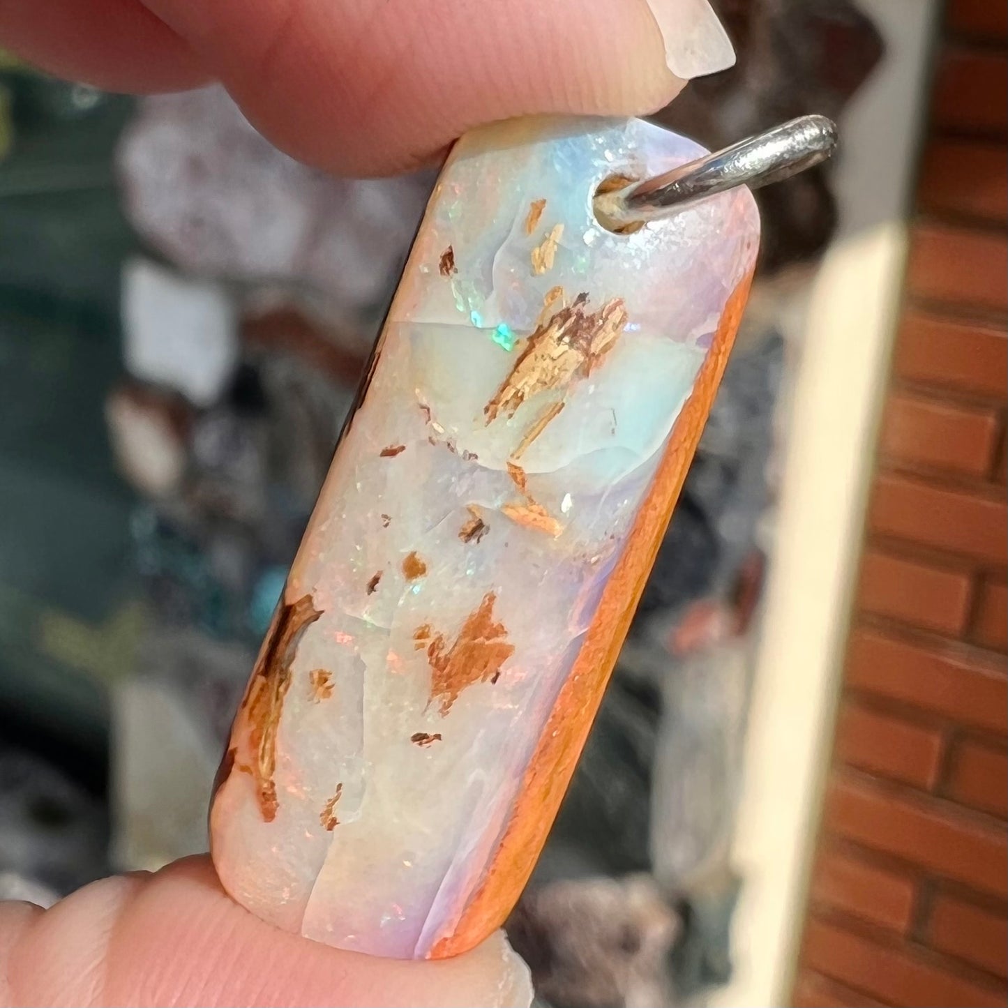 A drilled boulder opal stone with a sterling silver ring through the hole to be worn as a pendant.