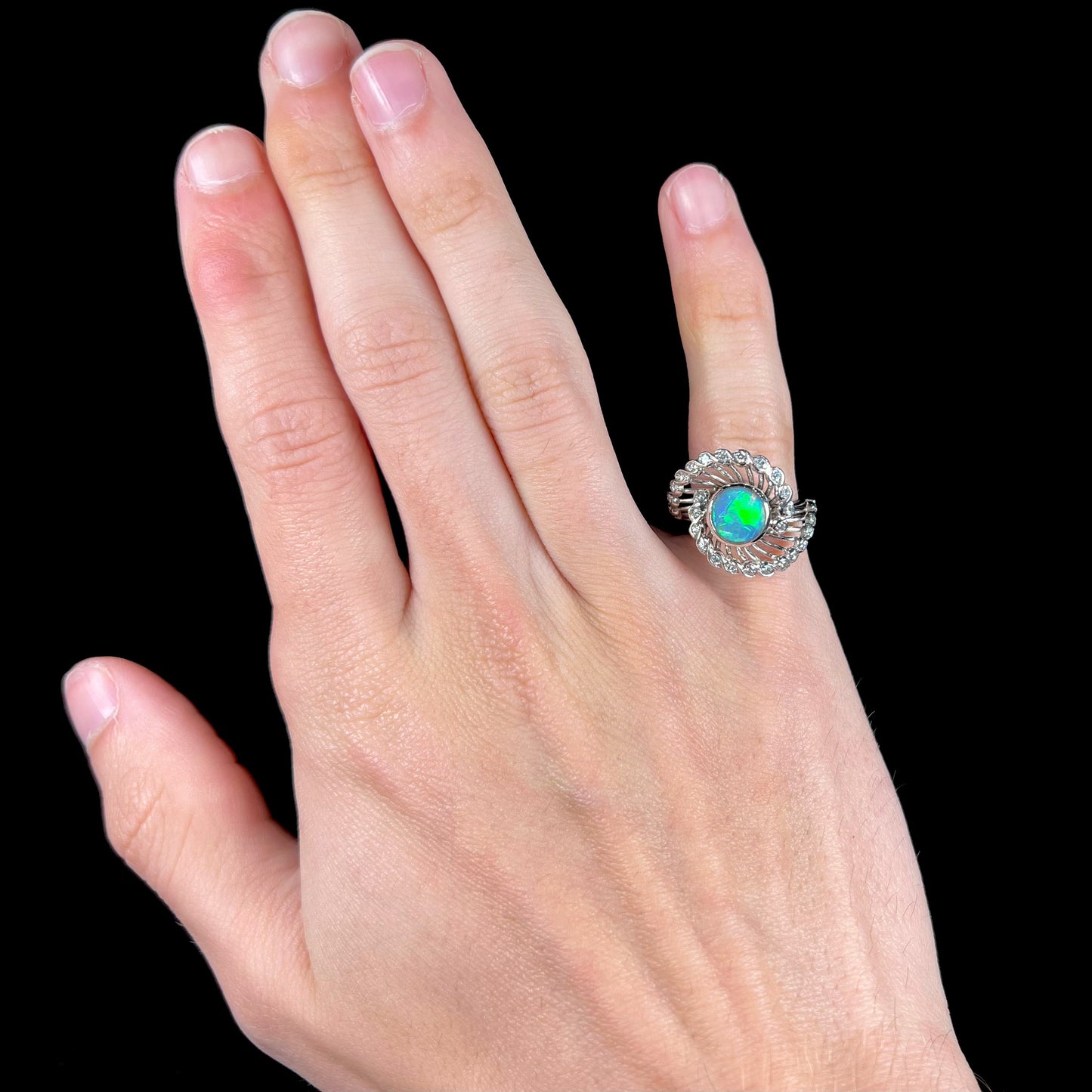 A white gold ring featuring a round cabochon cut black opal set in a swirl of round cut diamonds.