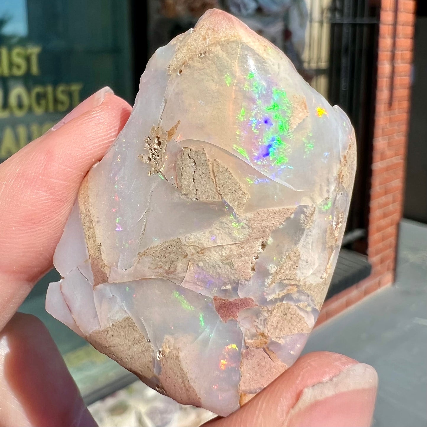 A preform polished matrix opal specimen from White Bluffs, Australia. Predominant colors are red, green, and violet.