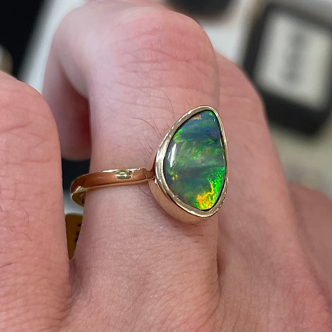A freeform cut semi-black opal from Lightning Ridge, Australia set in a bezel set yellow gold solitaire ring.